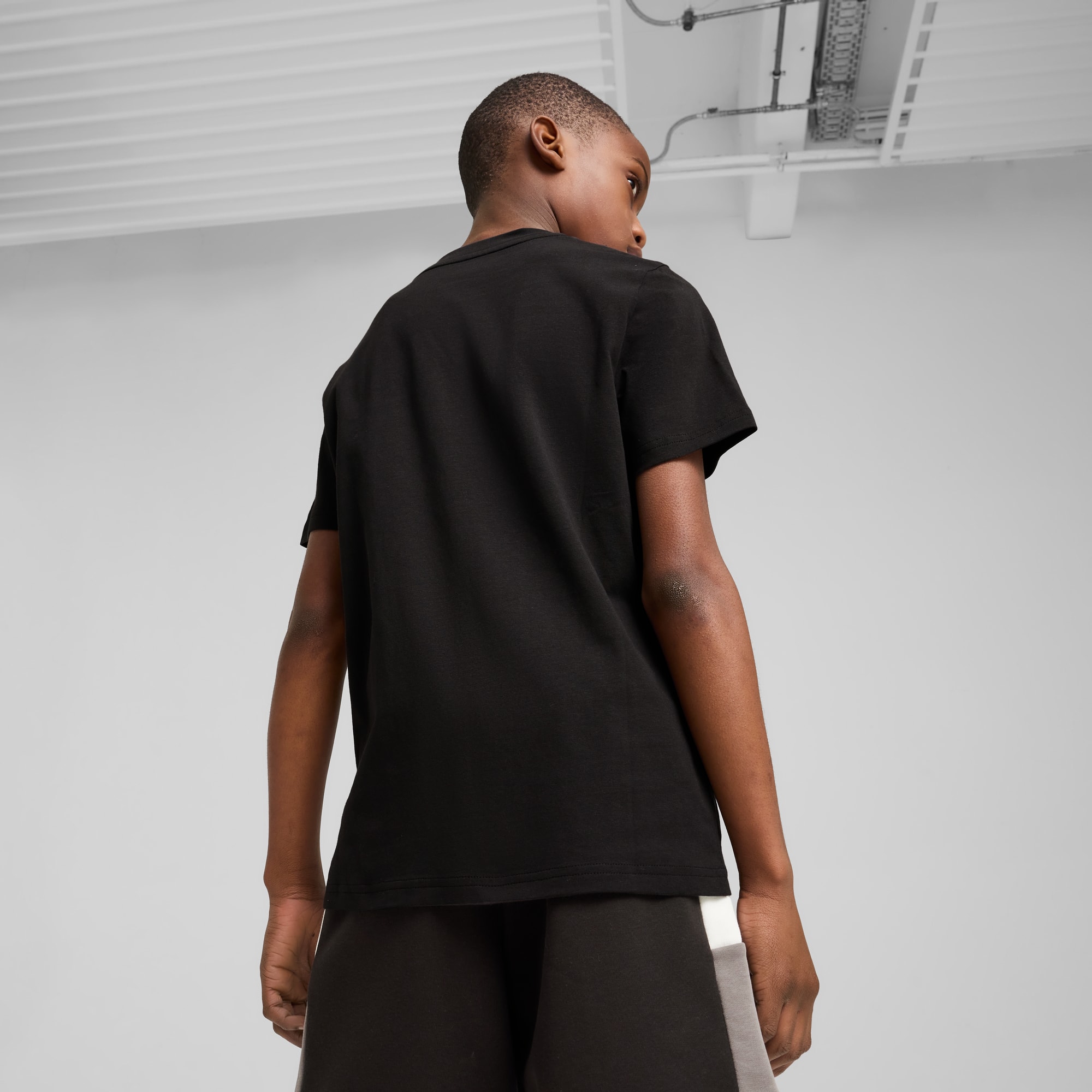 Un modello su sfondo grigio indossa una t-shirt nera e pantaloncini, guardando altrove.