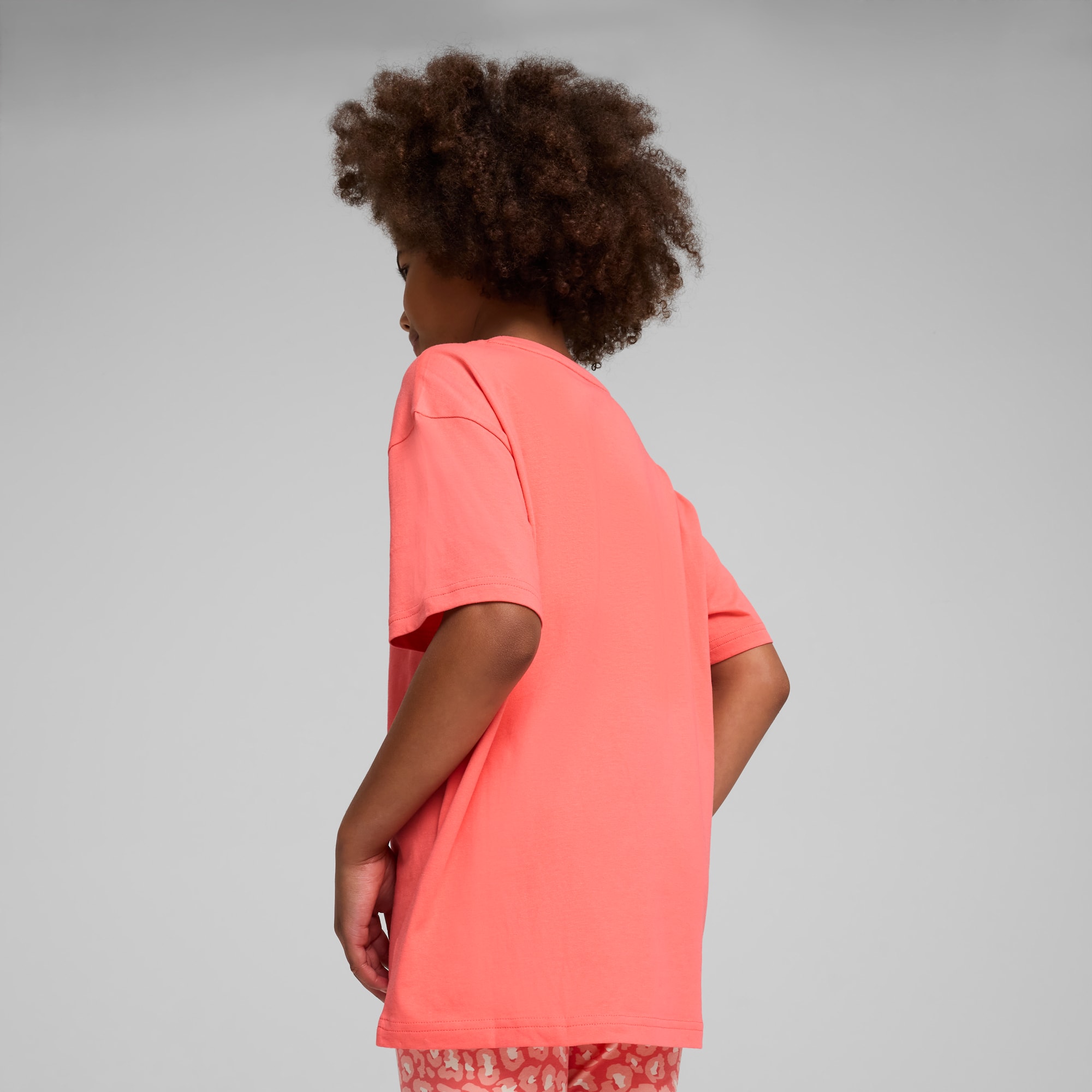 Sur fond gris, un enfant regarde vers le bas, vêtu d'un t-shirt rose et d'un bas rouge à motifs.