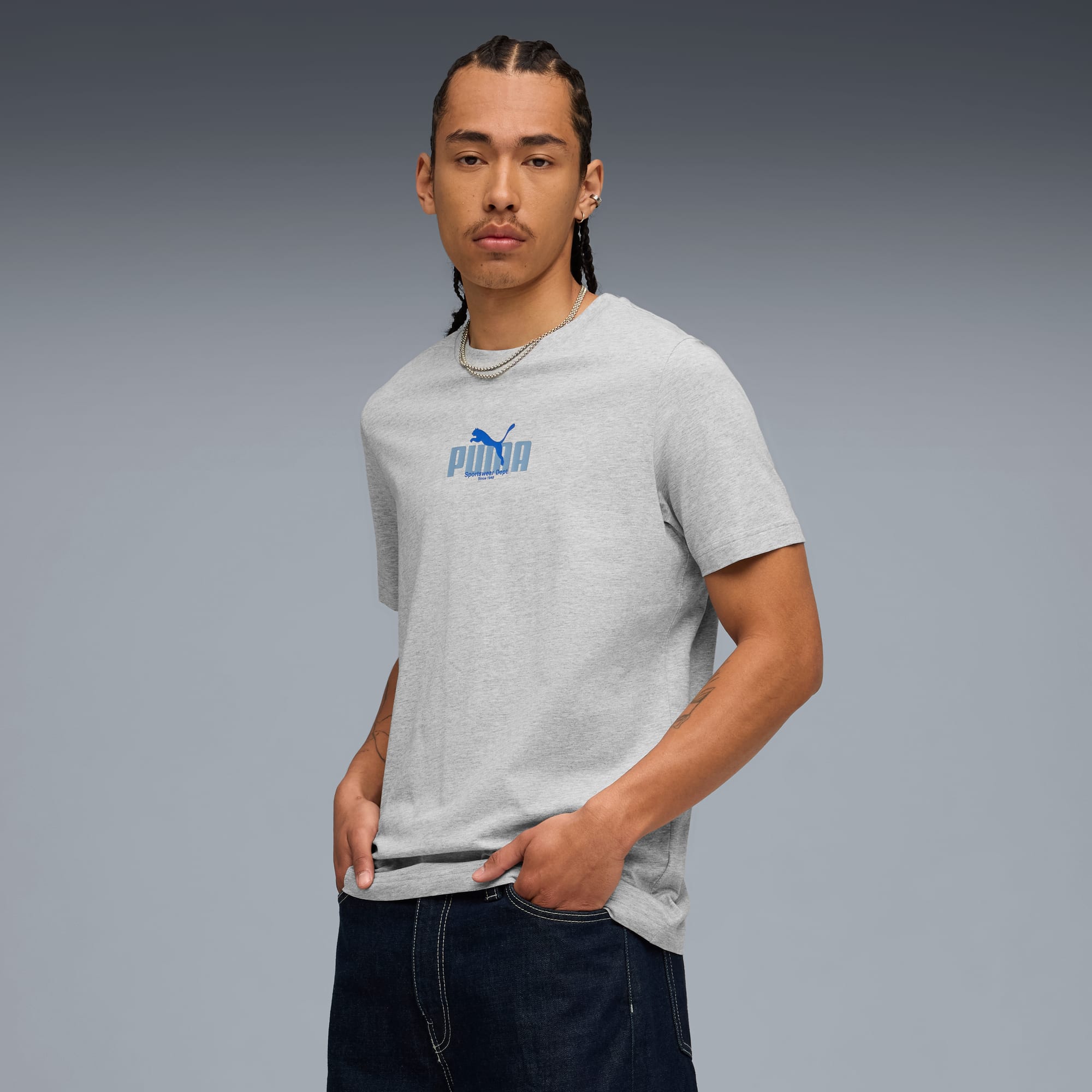 Op een grijze achtergrond poseert een model in een grijs t-shirt, met blauw logo en donkere jeans.