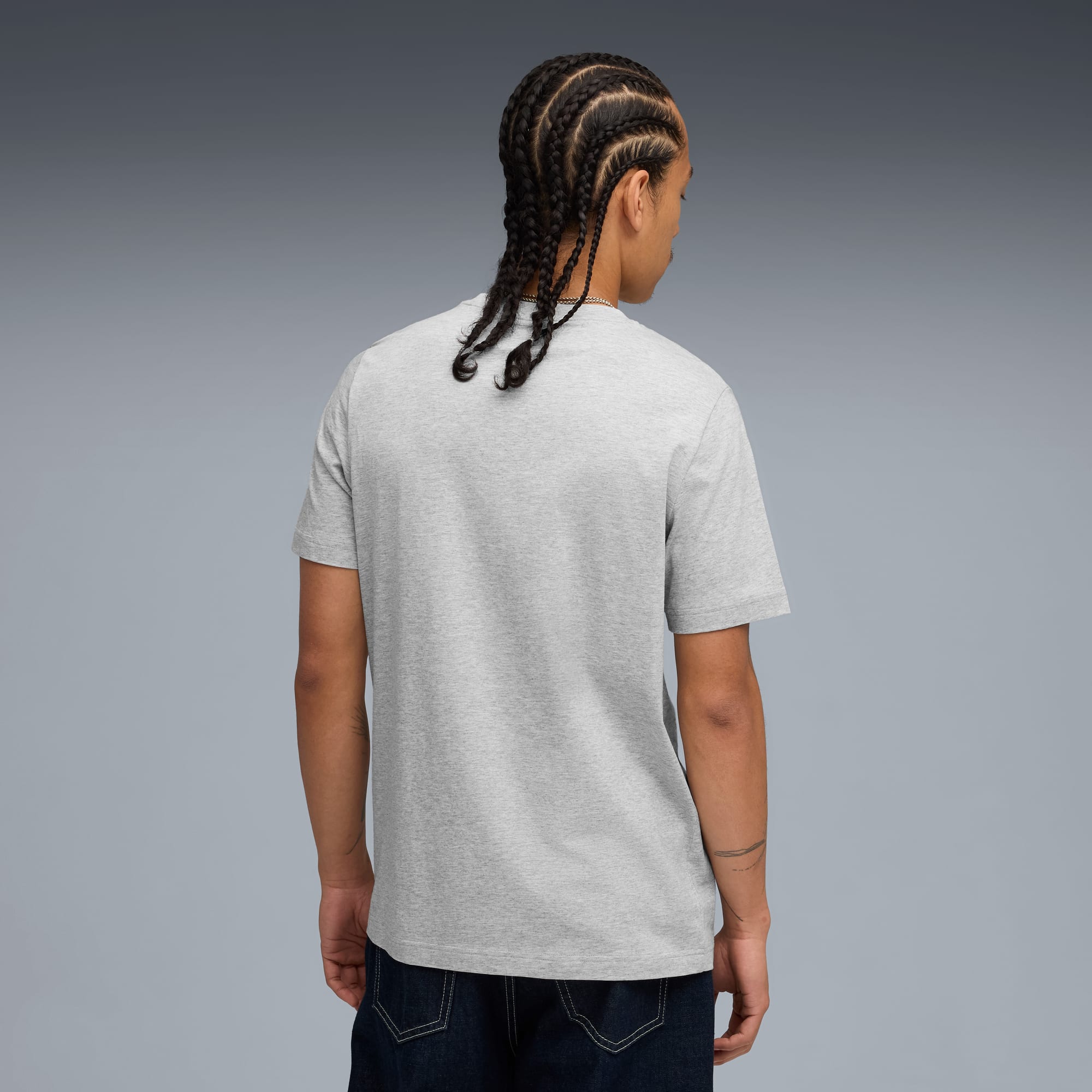 Een model met een grijs t-shirt en jeans staat met de rug naar de camera, tegen een grijze achtergrond.