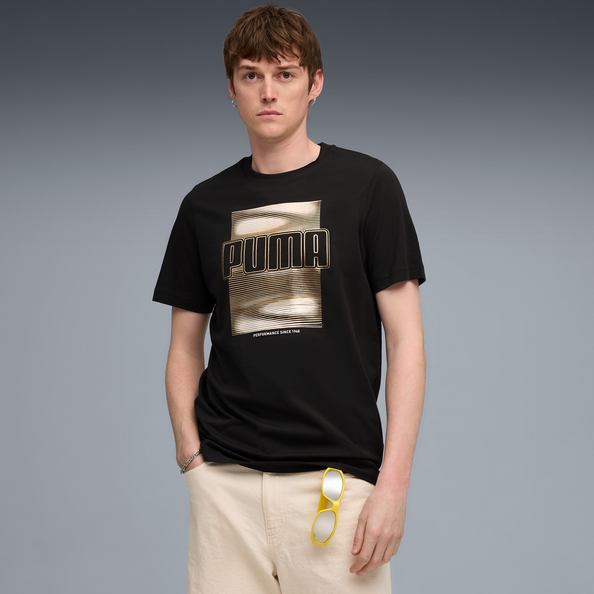 Tegen grijs poseert een model in een zwart Puma-shirt en een lichte short.