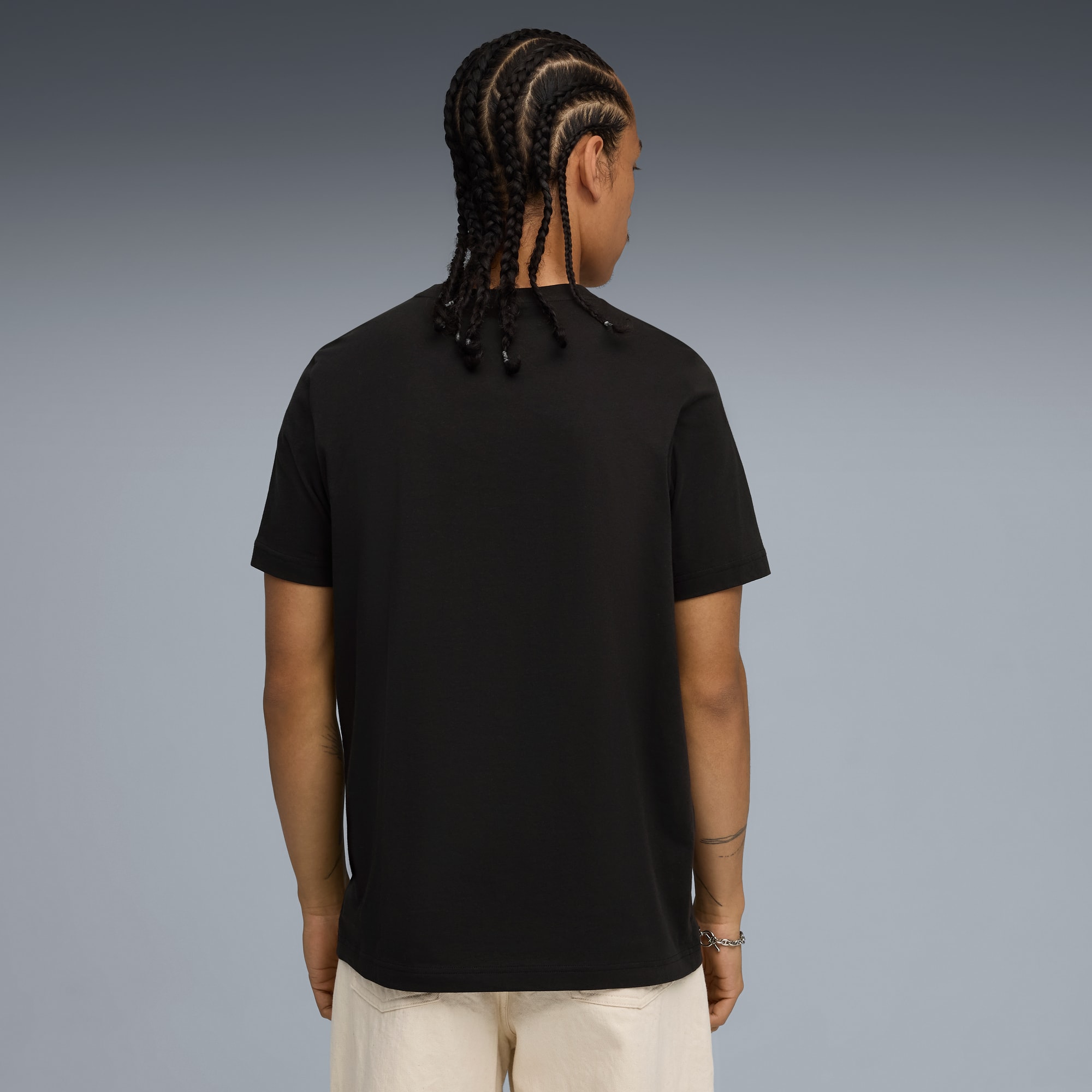 Un modèle, dos à la caméra sur fond gris, porte un t-shirt noir et un pantalon clair.