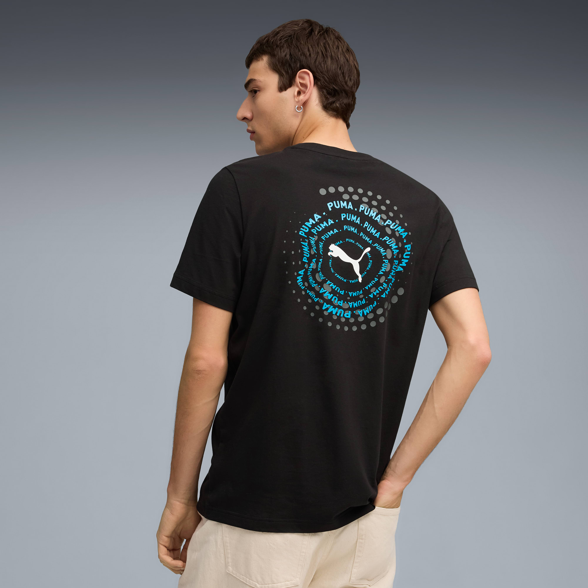 Een model staat met de rug naar de camera op grijs, draagt een zwart T-shirt met logo op de rug.