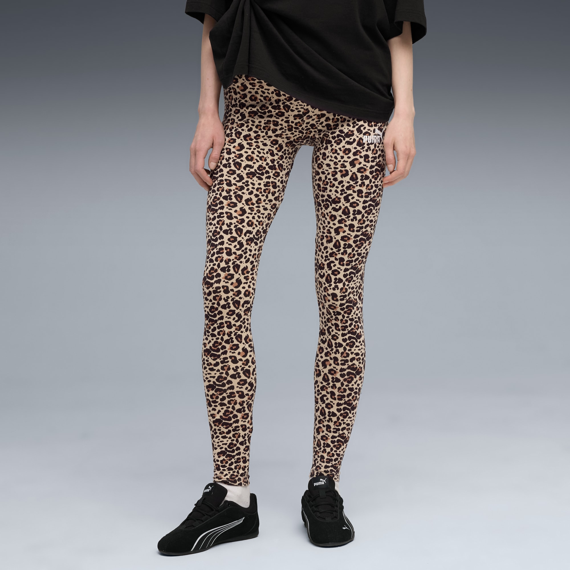 Tegen grijs draagt een model een luipaardprint legging en zwarte sportschoenen.