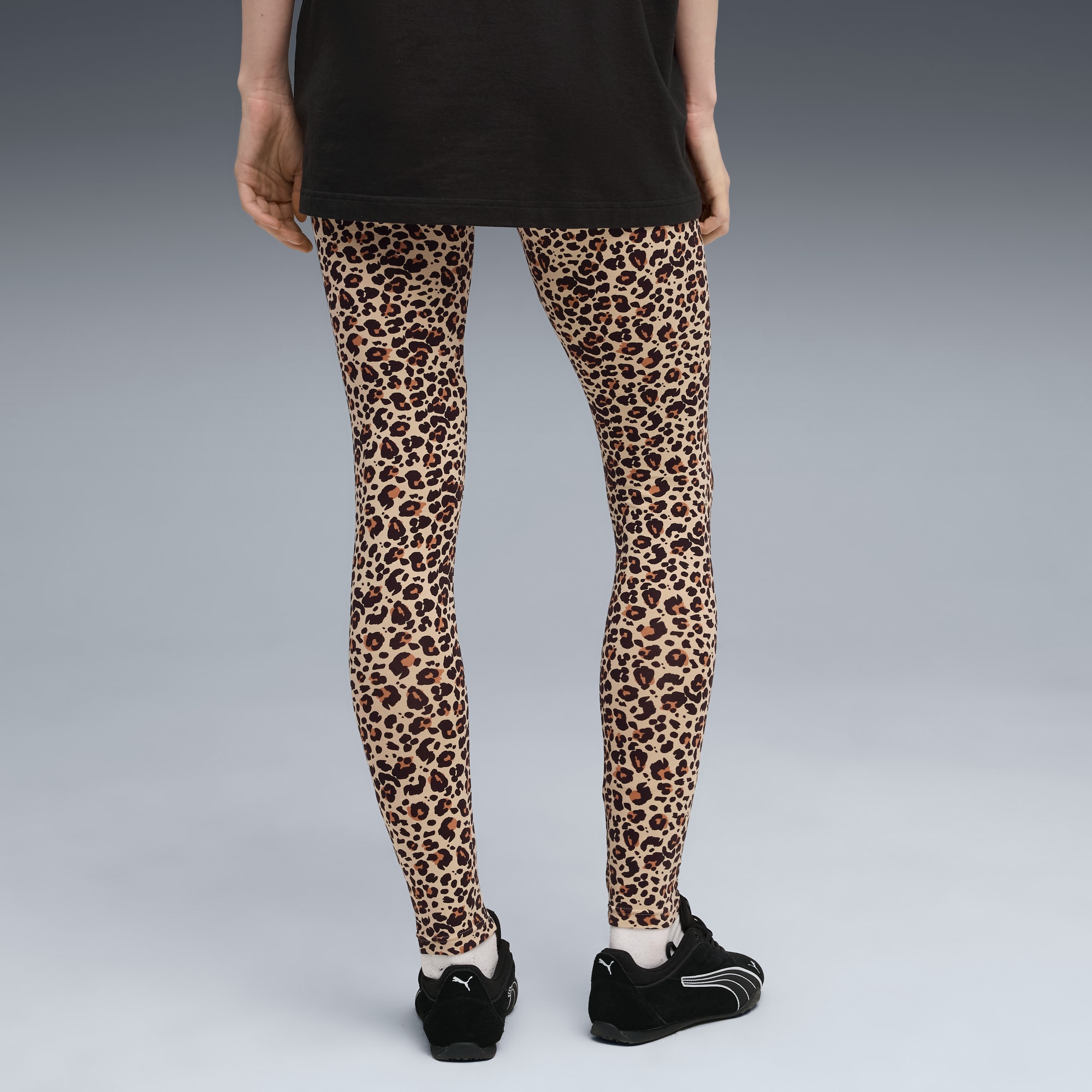 Een model staat tegen een grijze achtergrond met een dierenprint legging en zwarte sportschoenen.