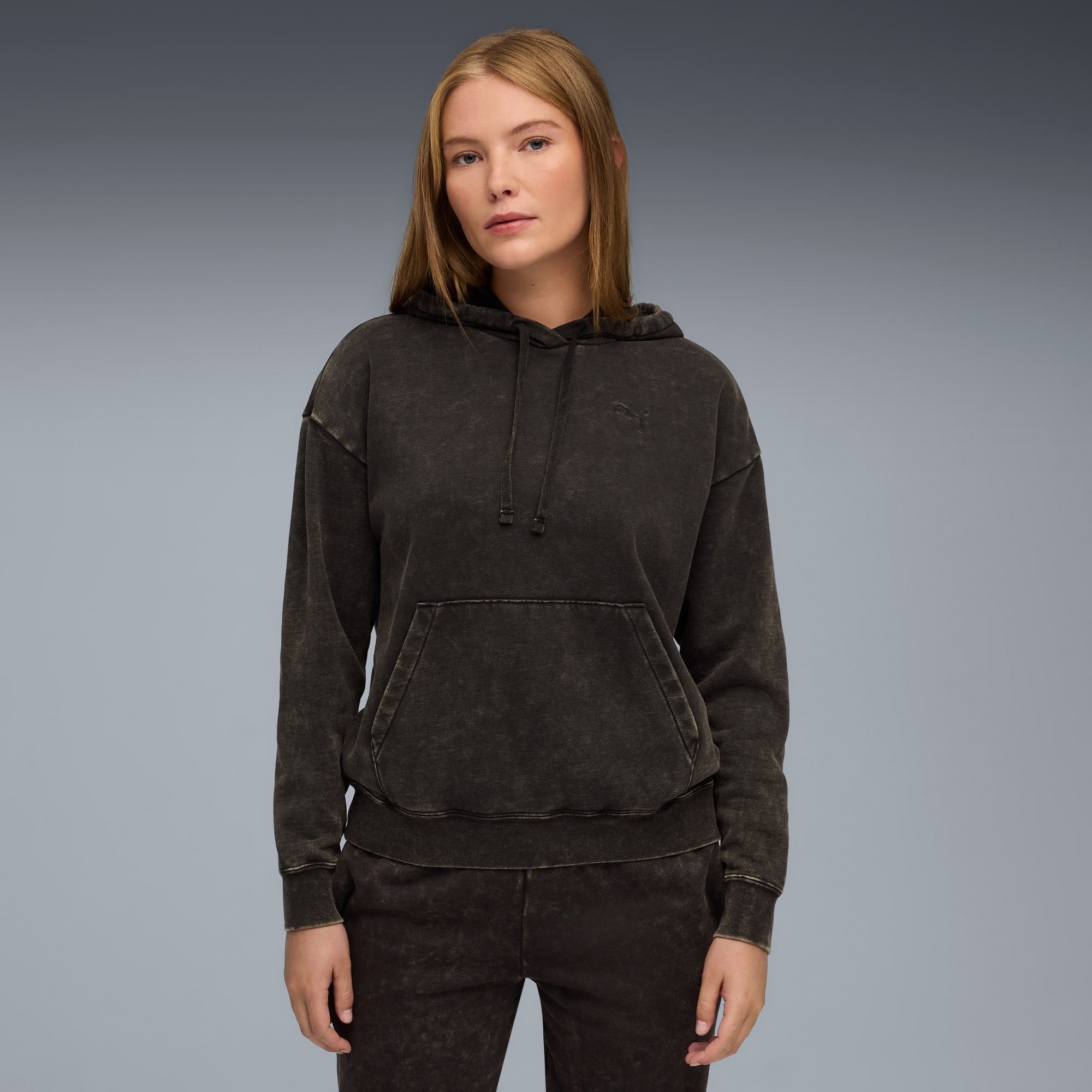 Un modèle pose sur un fond gris, portant un sweat à capuche foncé et un pantalon assorti.