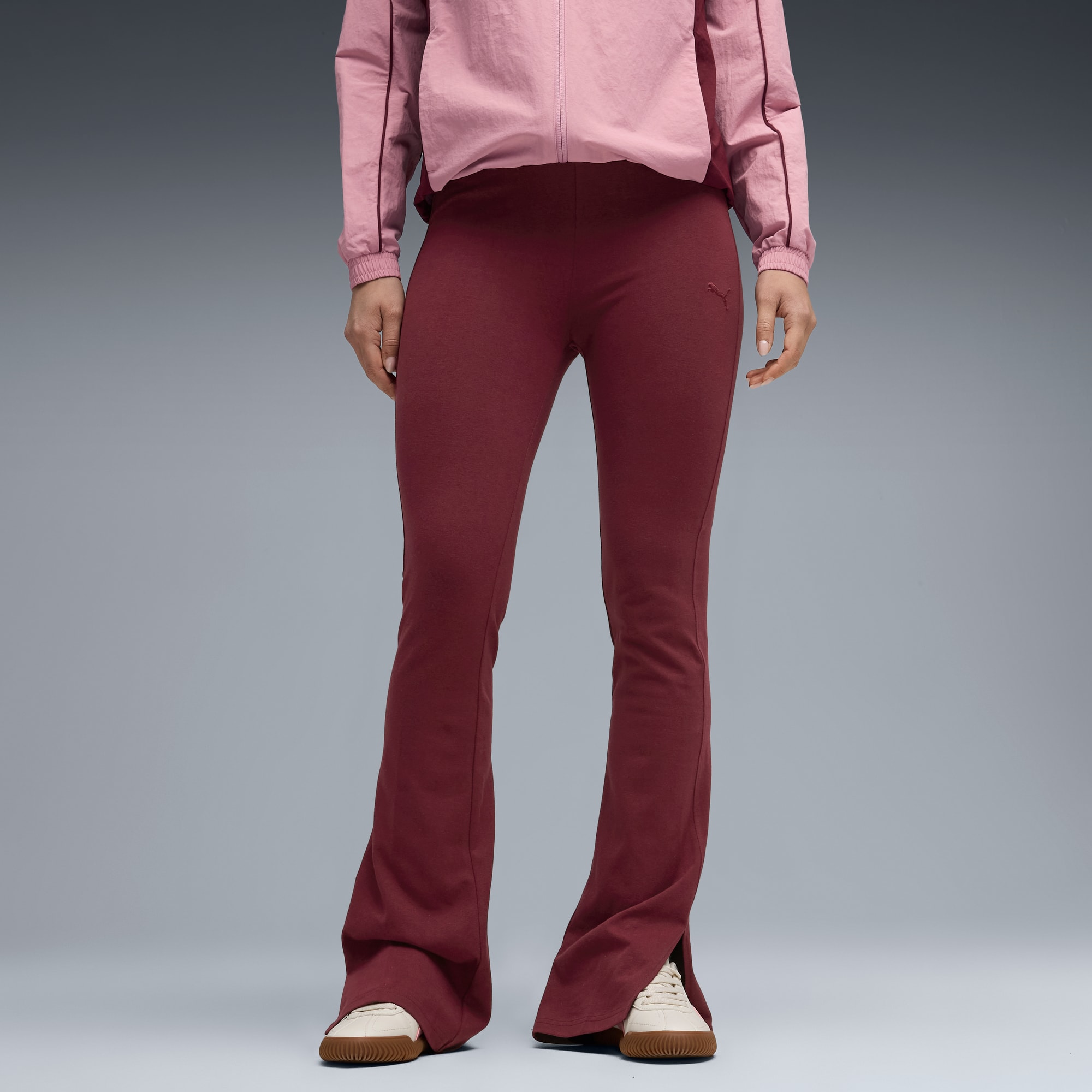 Ein Model posiert vor Grau, mit pinkfarbener Jacke, weinroter Hose und cremefarbenen Turnschuhen.