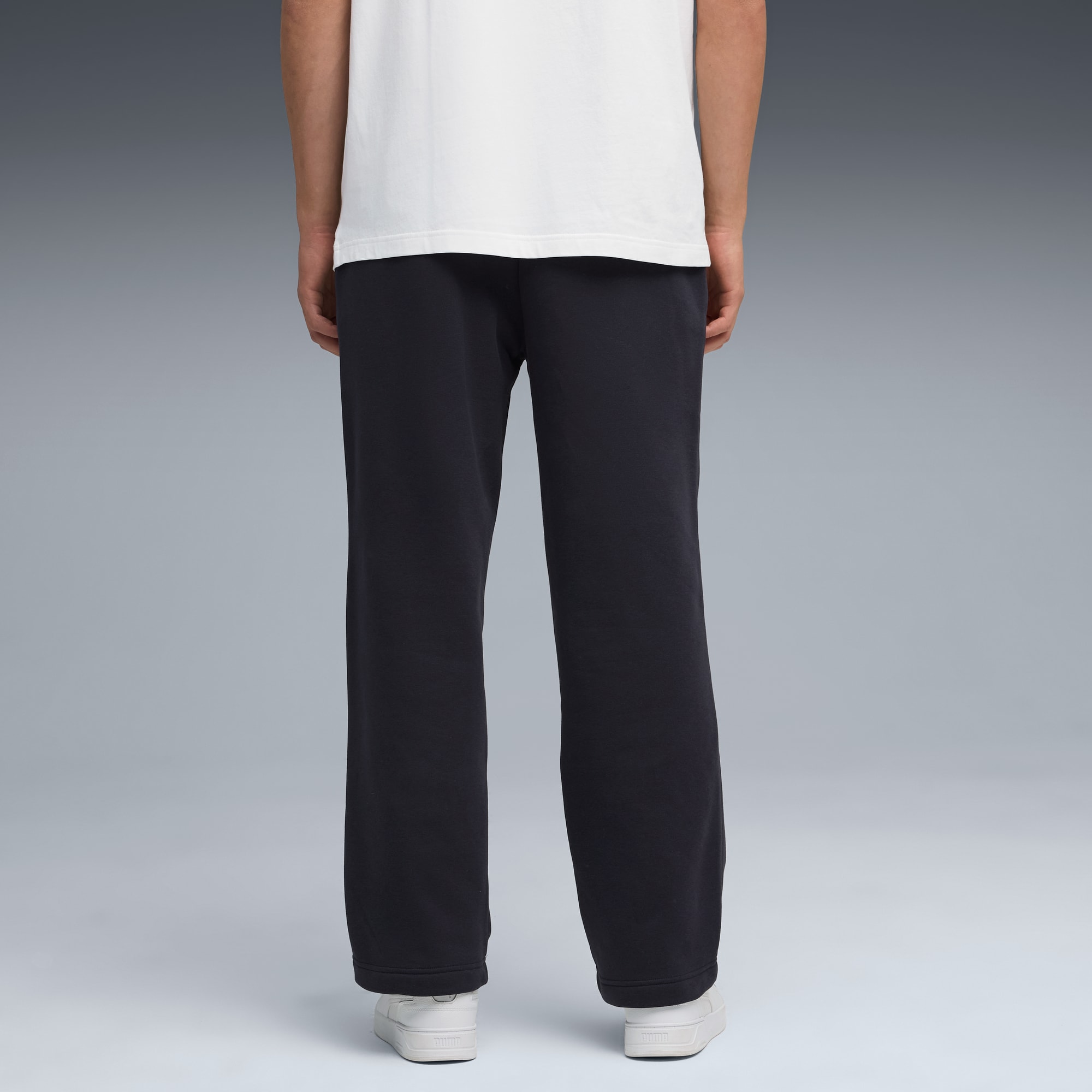 Model, rugzijde, op grijs, met wit shirt, donkere broek en sportschoenen.