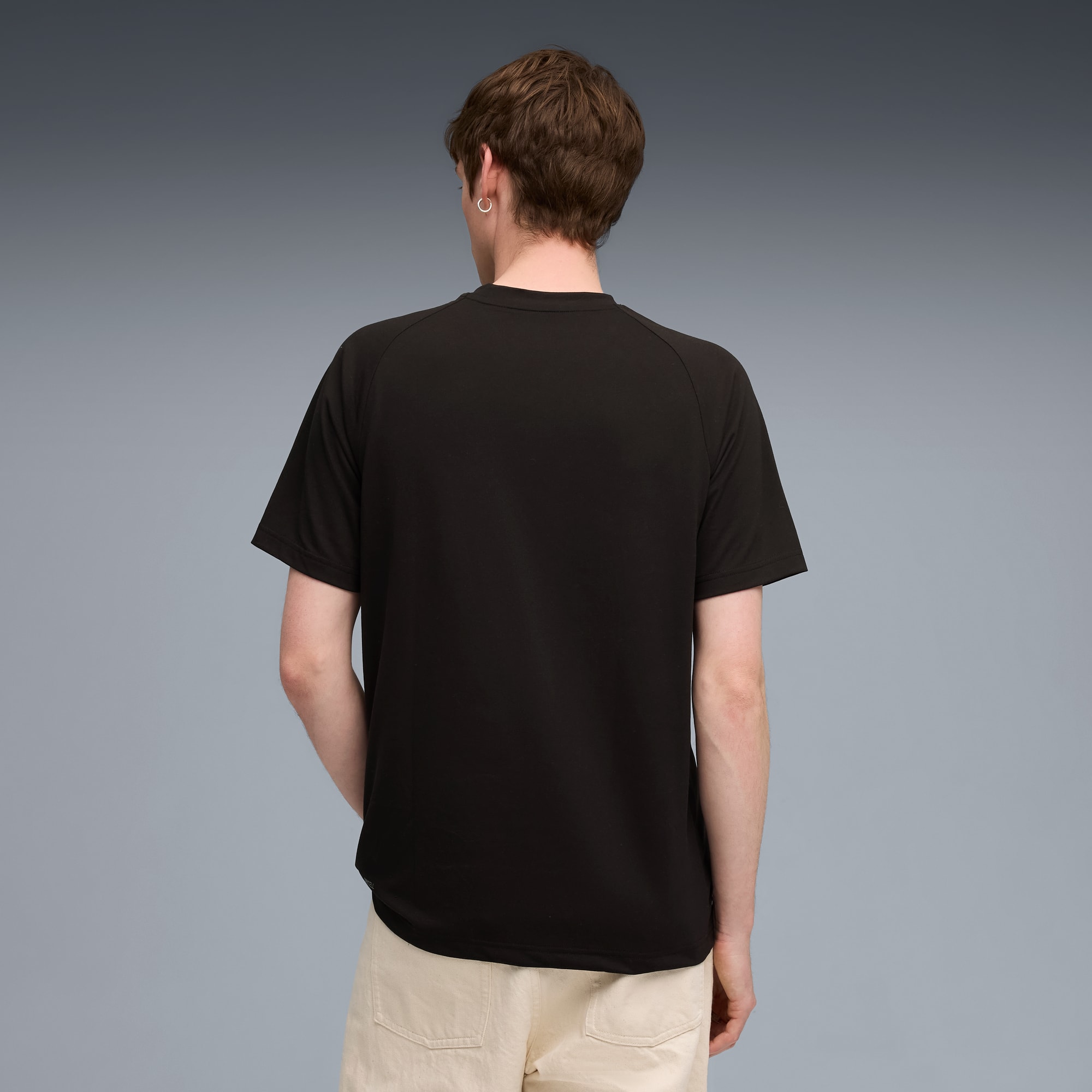 Ein Model mit schwarzem T-Shirt und hellen Shorts vor grauem Hintergrund, abgewandt.