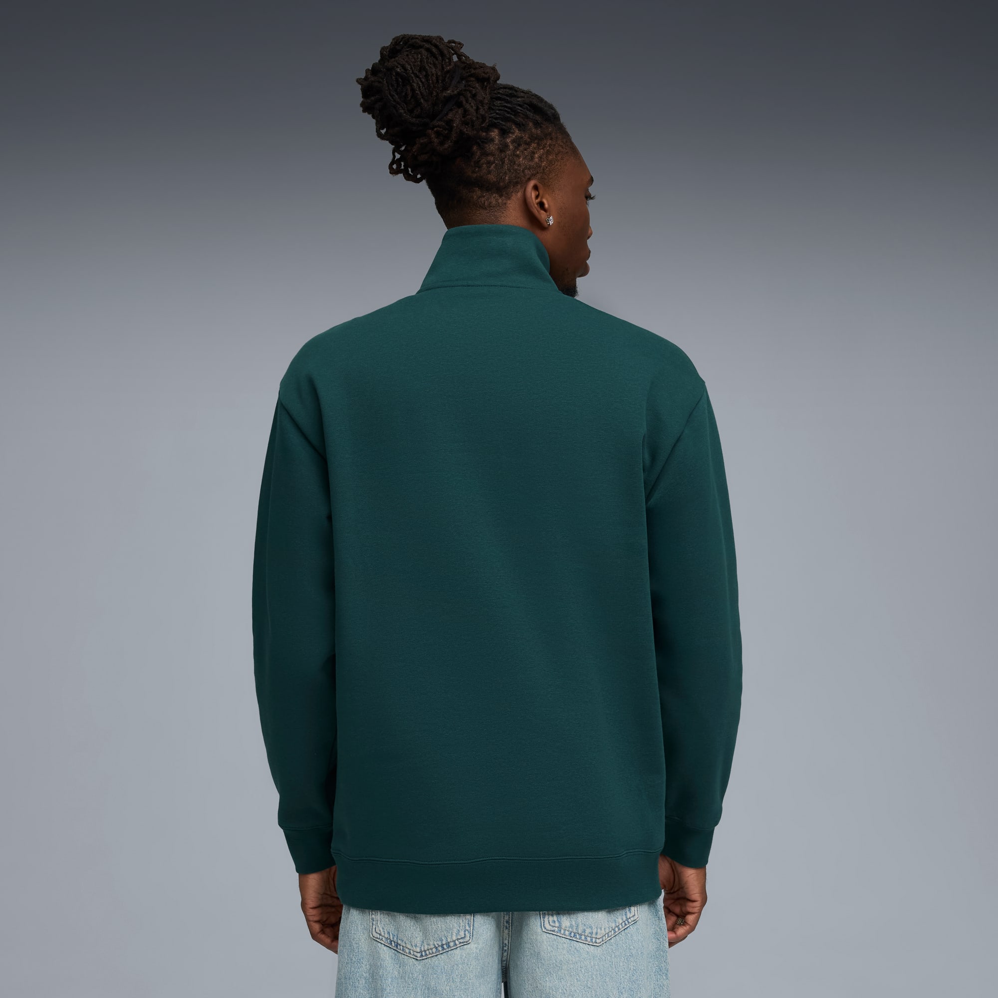 Un modello di spalle indossa una felpa verde e jeans chiari su sfondo grigio.