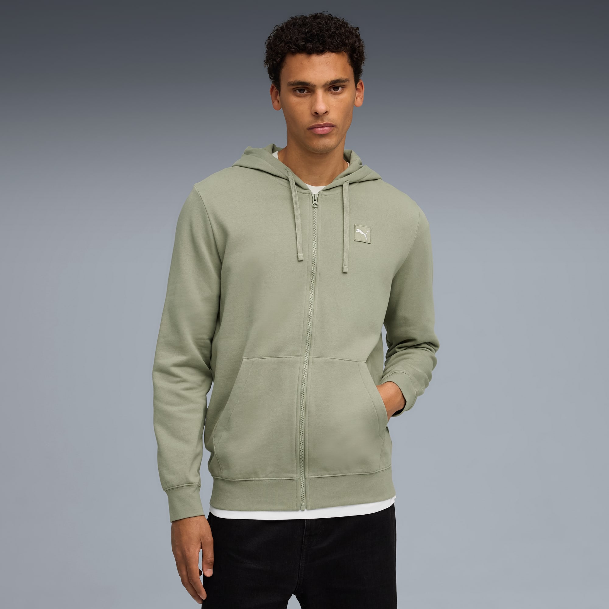 Sur fond gris, un mannequin porte un sweat à capuche zippé sauge, un t-shirt blanc et un jean.