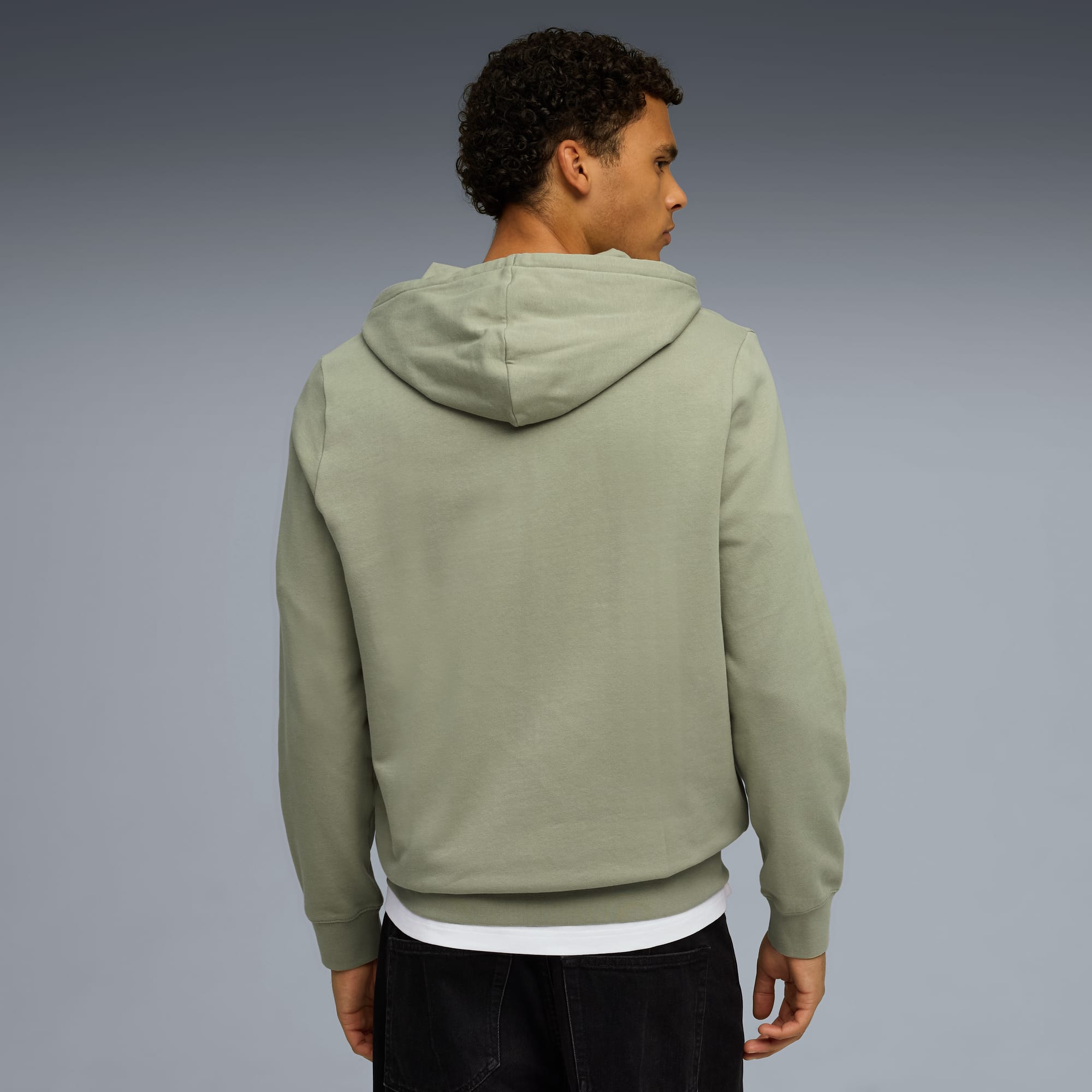 Un modèle, dos à l'objectif sur fond gris, porte un sweat à capuche sauge, un t-shirt et un jean.