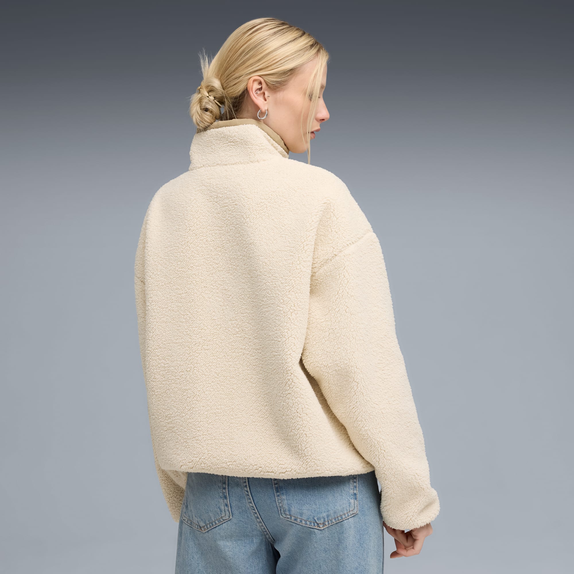 Ein Model vor grauem Hintergrund, von hinten in einem cremefarbenen Fleece und blauen Jeans.