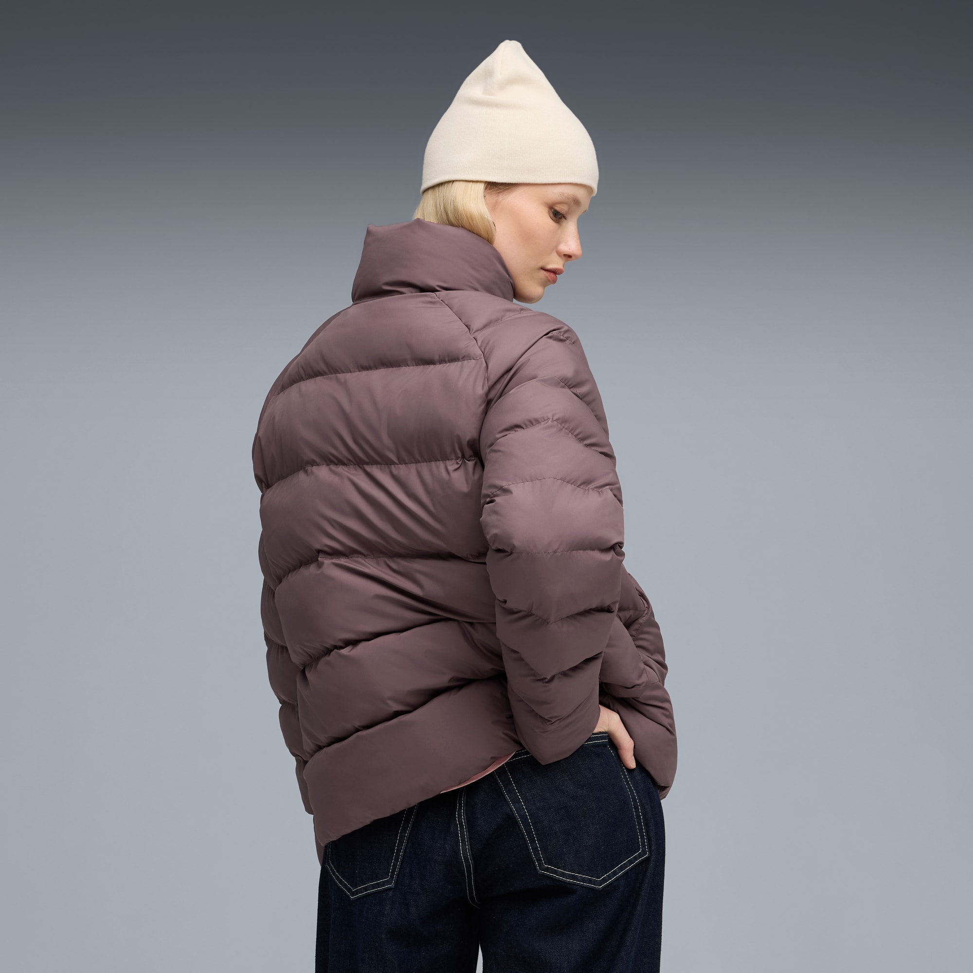 Un modello su sfondo grigio indossa un piumino, jeans e un berretto.