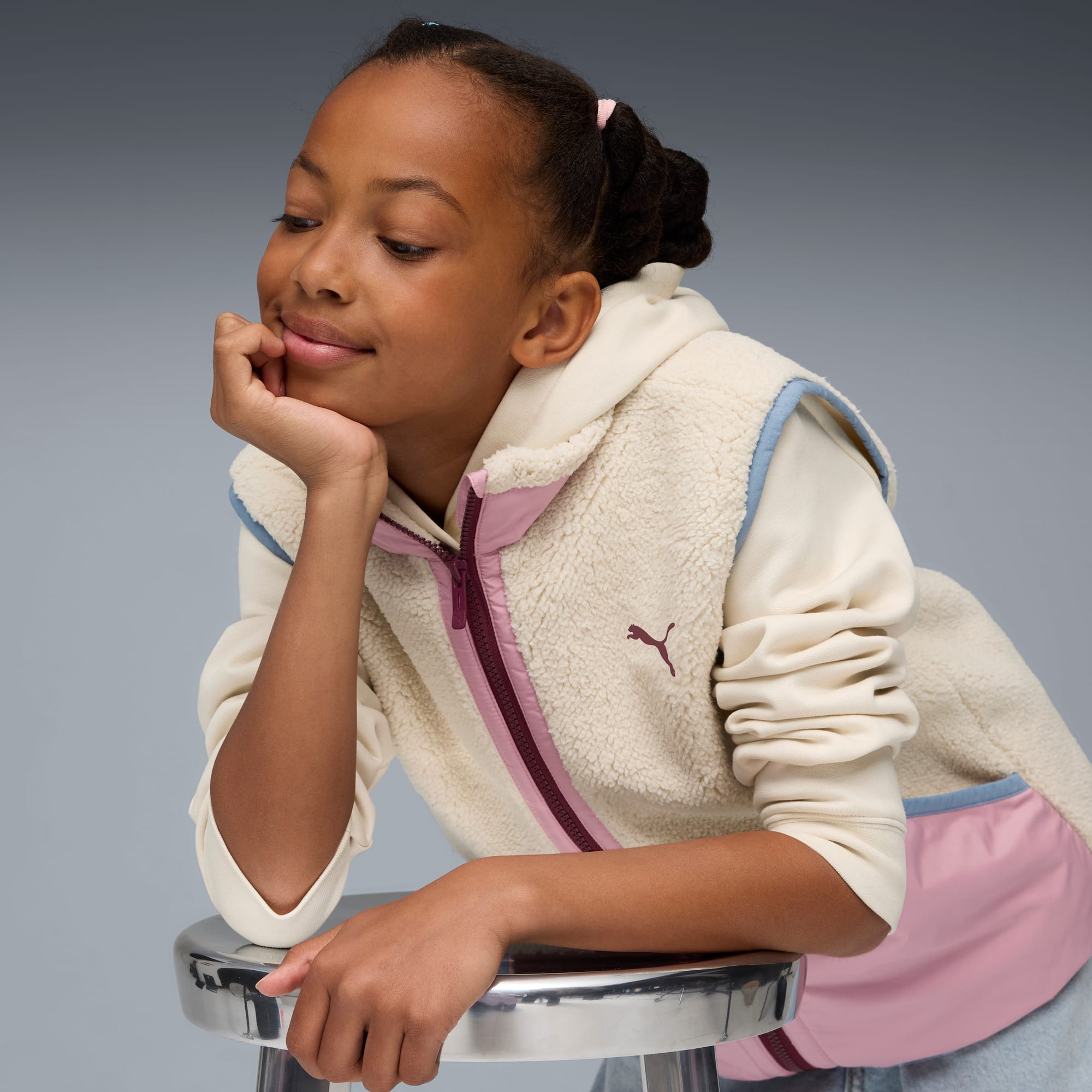 Een kind rust met haar hoofd op haar hand, terwijl ze een crème fleece vest met roze accenten draagt.
