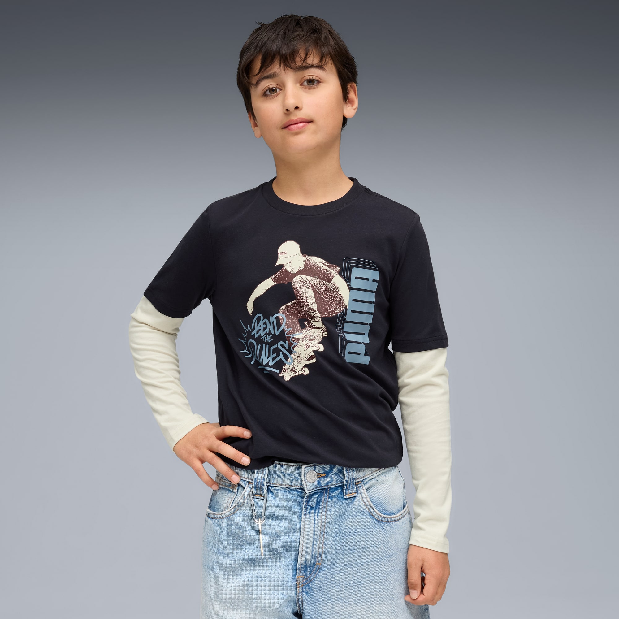 Een model op een grijze achtergrond draagt een zwart T-shirt met skaterafbeelding en lichtblauwe jeans.