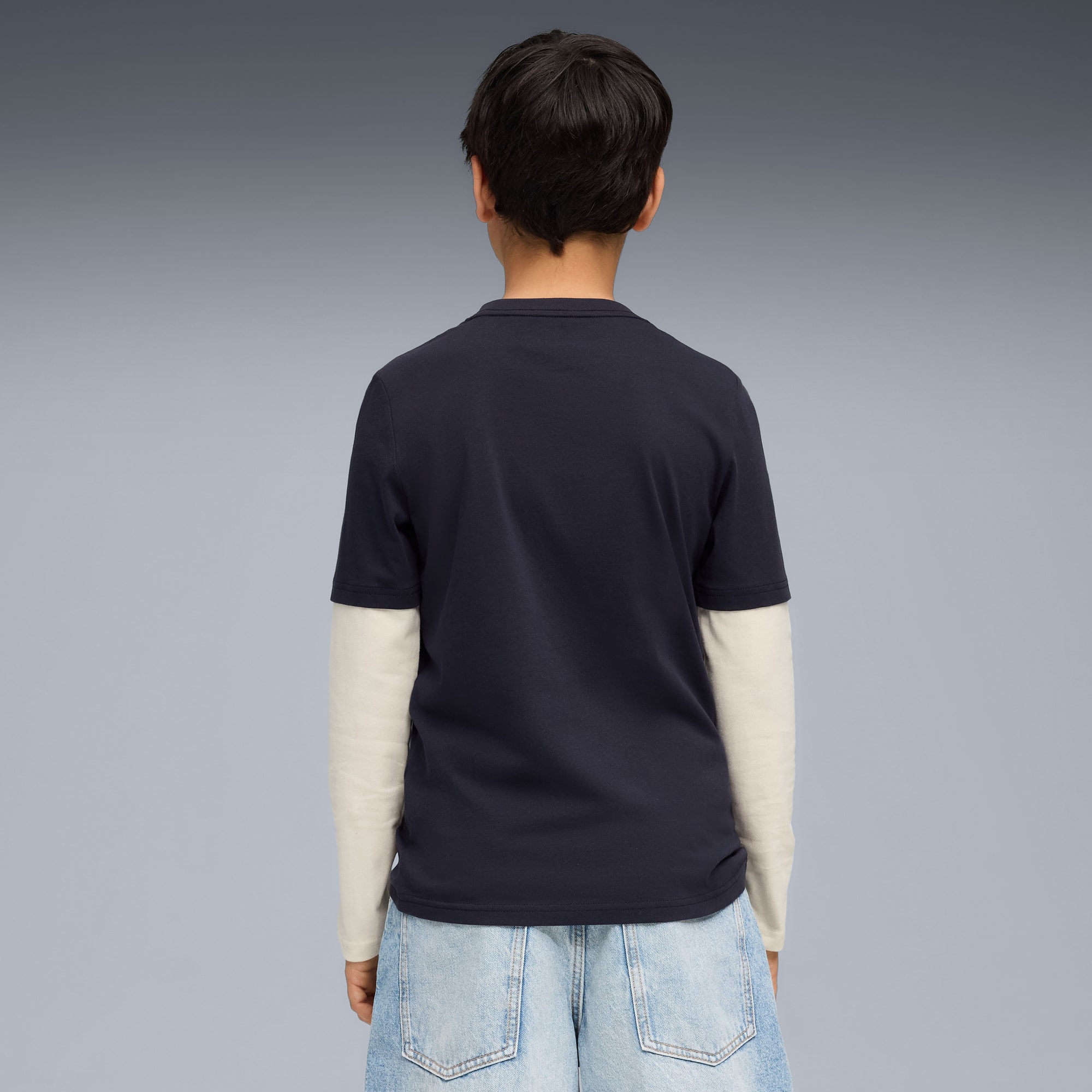 Een model staat met de rug naar de camera op een grijze achtergrond, gekleed in een marineblauw T-shirt.