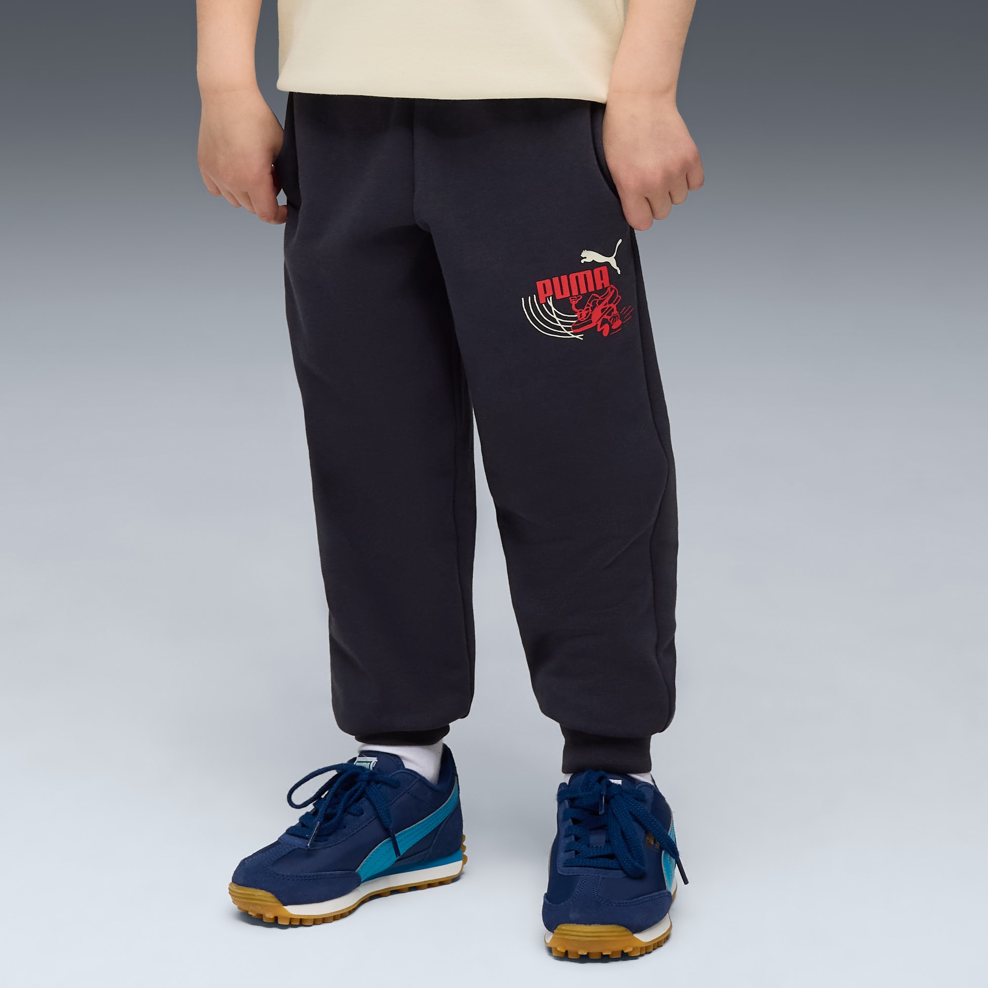 Un modello indossa pantaloni da jogging scuri con logo e scarpe da ginnastica blu su sfondo grigio.