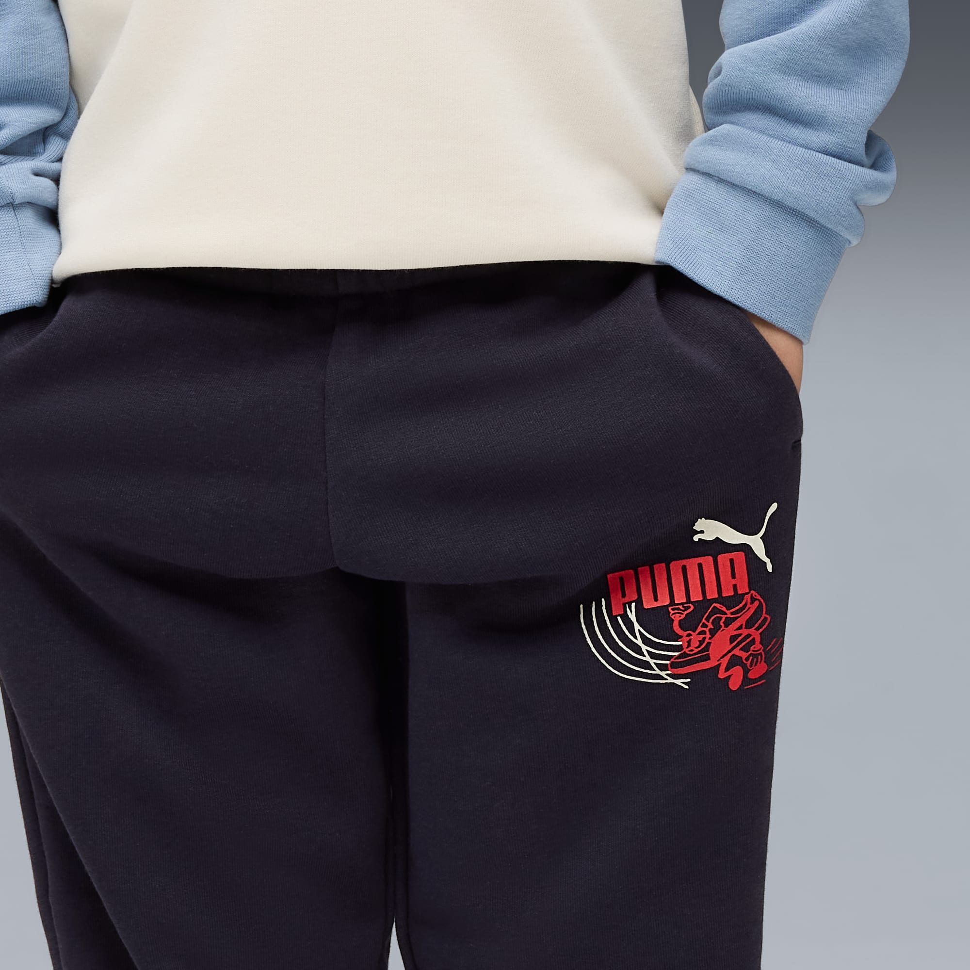 Su sfondo grigio, una persona indossa pantaloni da jogging blu navy con logo Puma colorato.