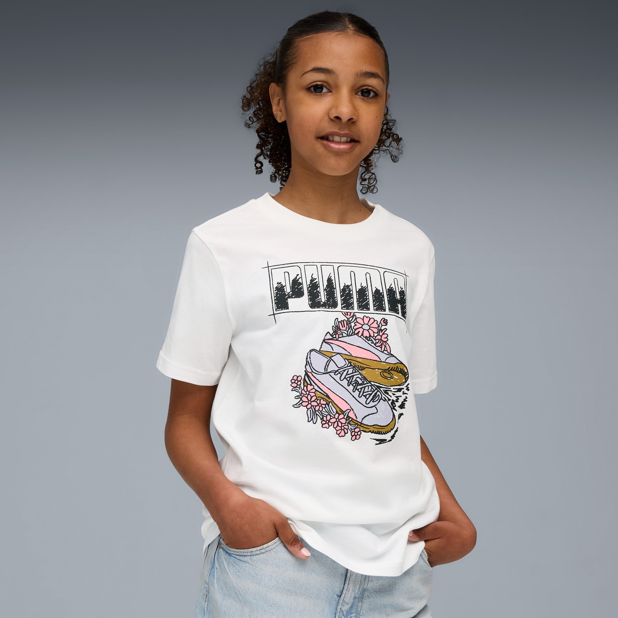 Een model poseert tegen grijs, in een wit grafisch T-shirt en lichte denim broek.