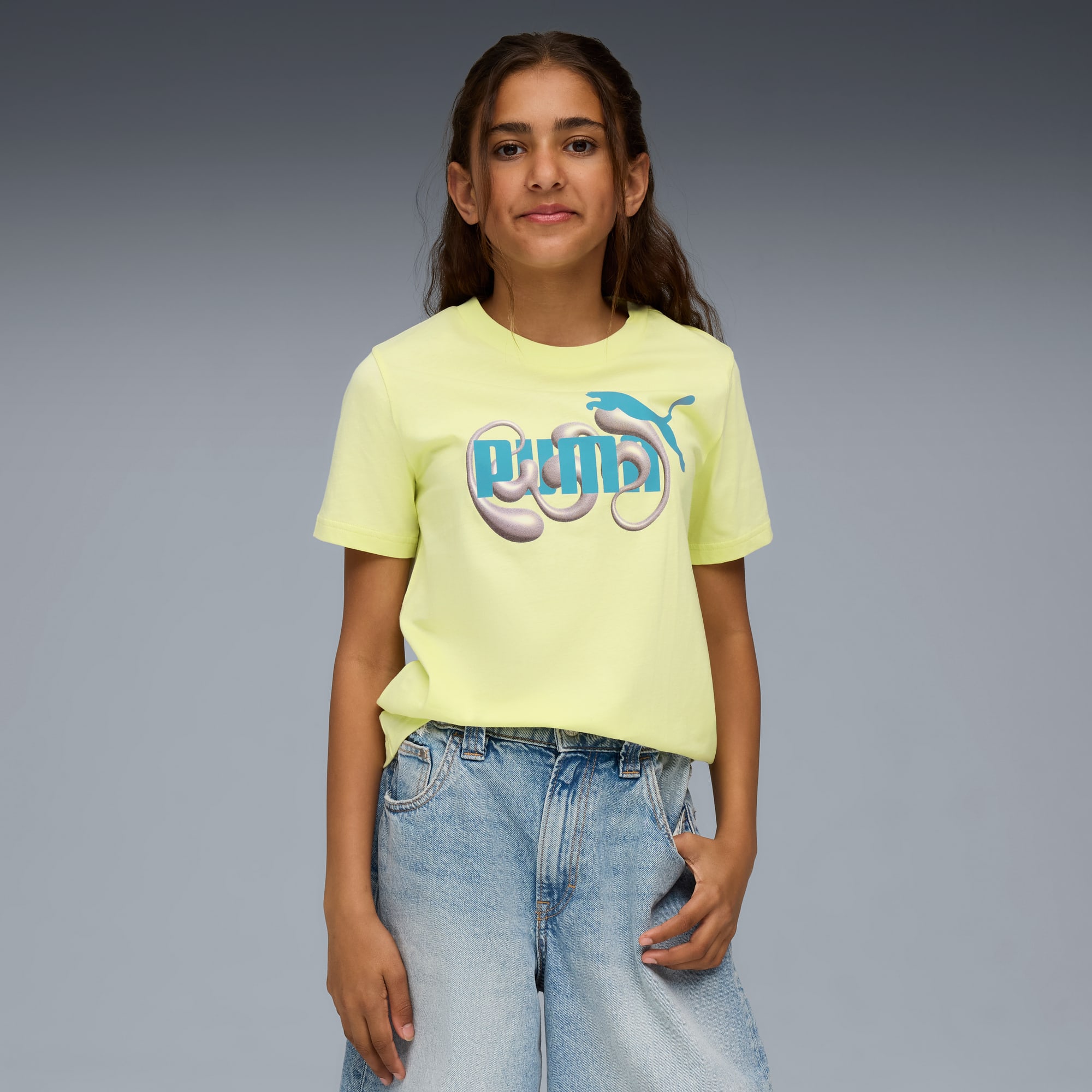 Ein Model steht vor grauem Hintergrund in gelbem T-Shirt und Jeansshorts.