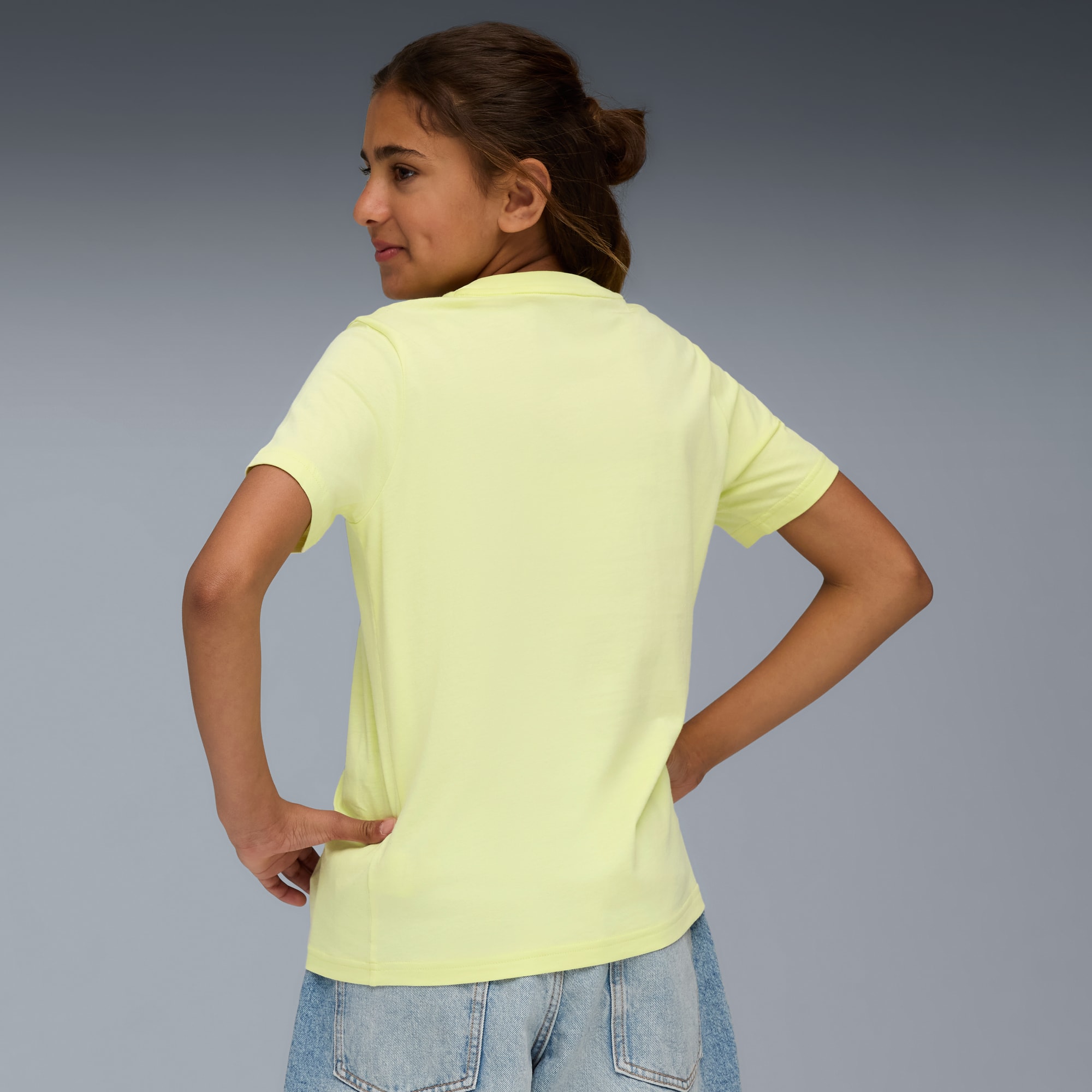 Ein Model posiert vor grauem Hintergrund, mit gelbem T-Shirt und Jeansshorts.