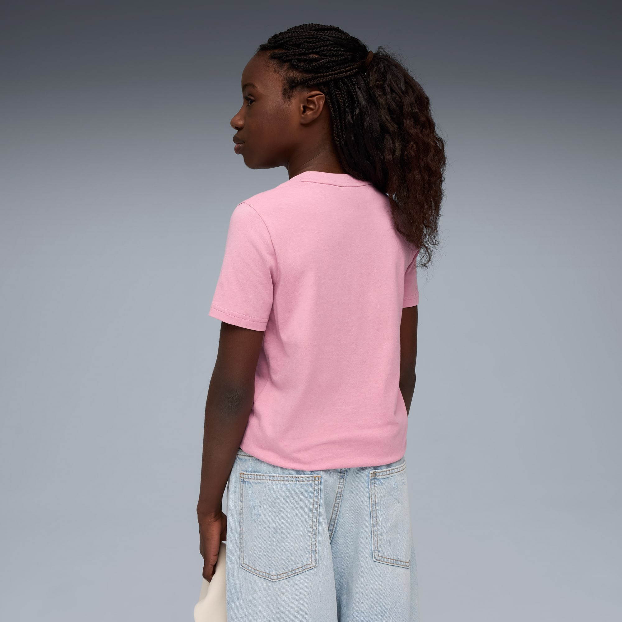 Su sfondo grigio, una modella di profilo indossa una t-shirt rosa e jeans azzurri.