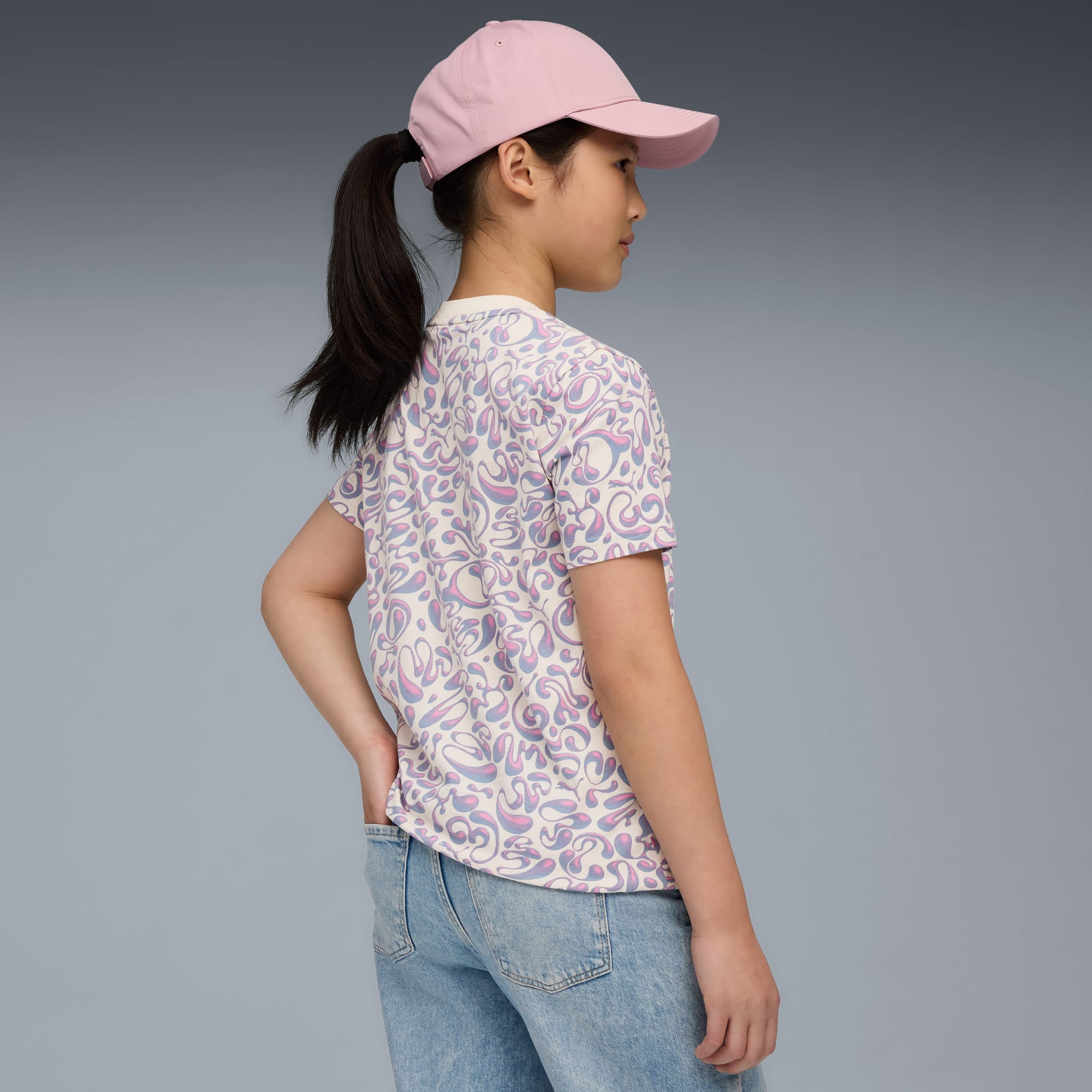 Een model voor een grijze achtergrond, met een T-shirt met patroon, jeans en een roze pet.