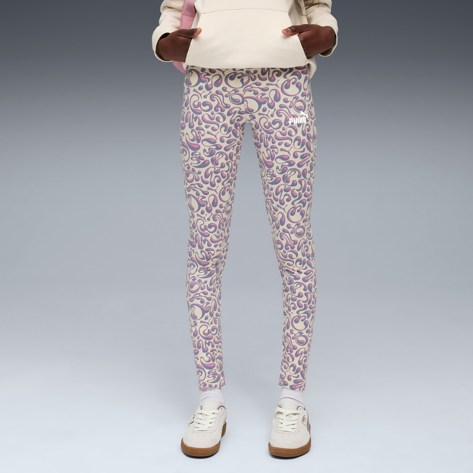 Un mannequin sur fond gris porte un legging à motifs, un sweat à capuche et des baskets.