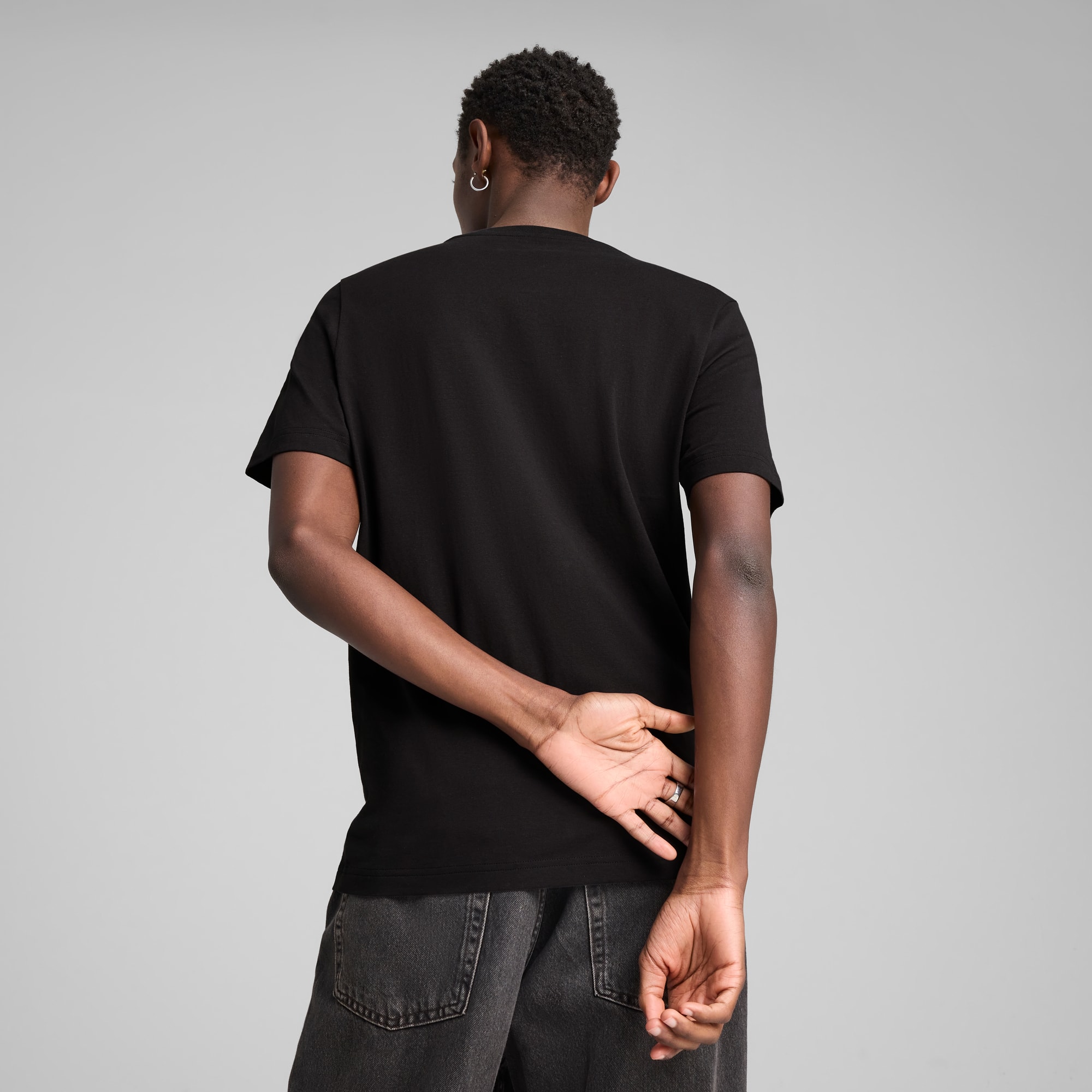 Un modèle, de dos, porte un t-shirt noir et un jean gris sur fond gris.