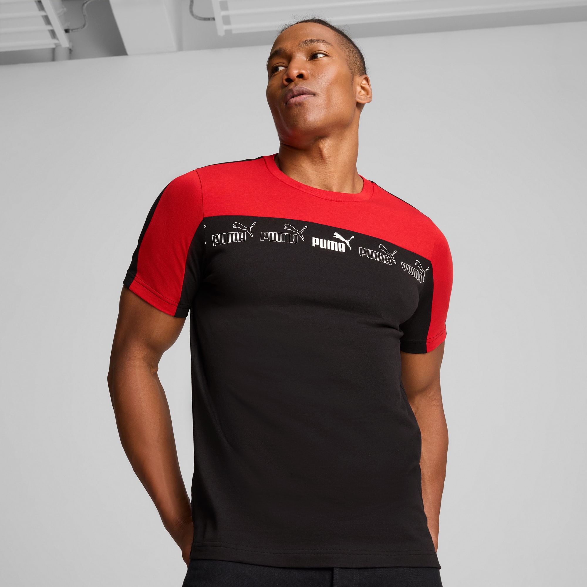 Tegen een grijze achtergrond poseert een model in een zwart en rood Puma T-shirt.