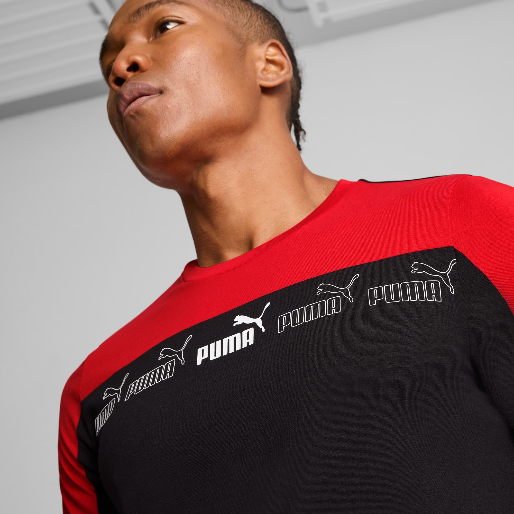 Een model poseert tegen een grijze achtergrond, gekleed in een zwart-rode Puma longsleeve.