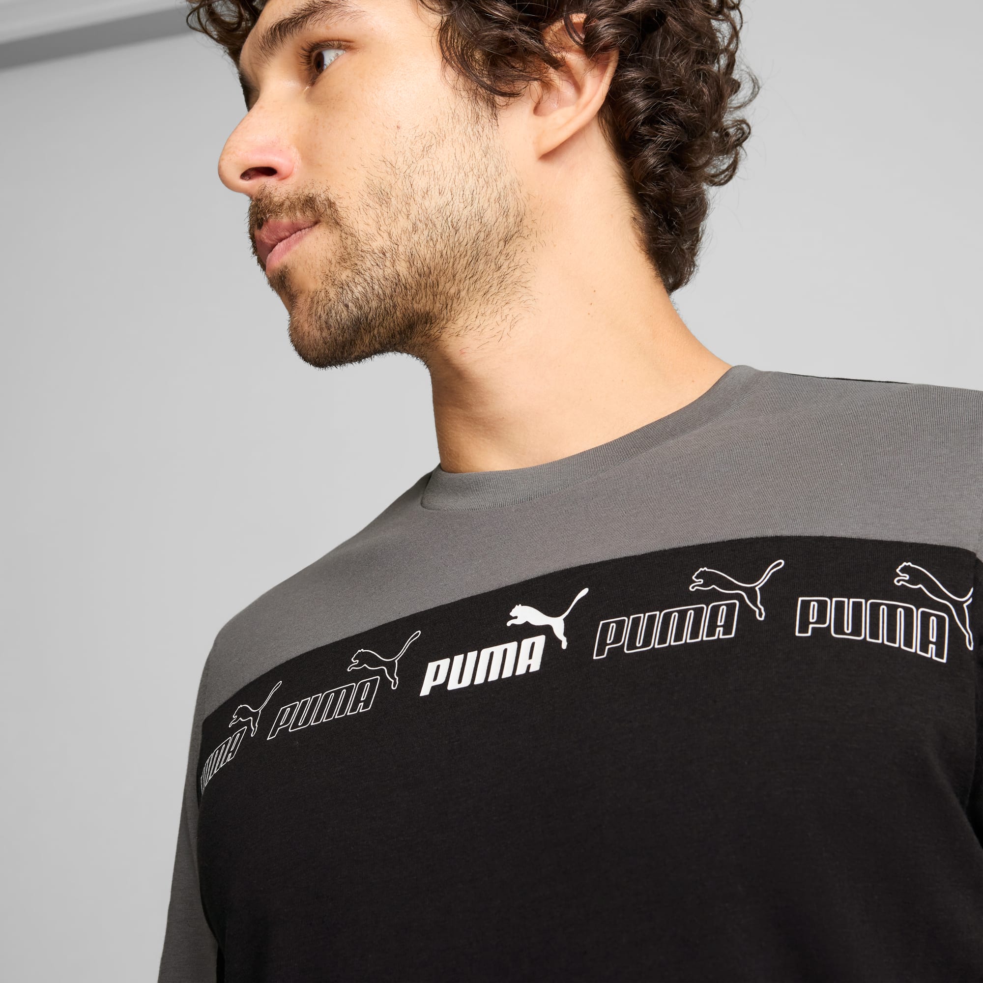 Een model poseert tegen grijs, gekleed in een grijs en zwart Puma shirt met lange mouwen.