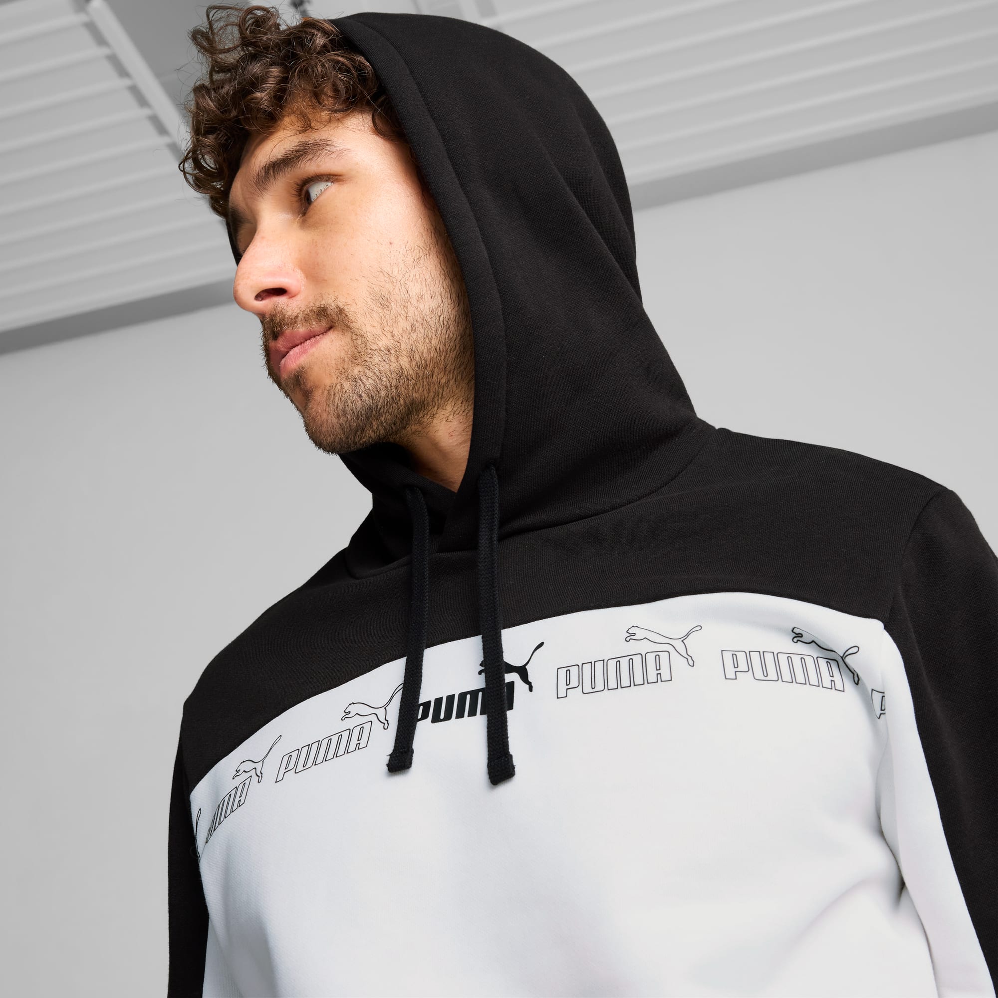 Un modèle pose sur fond gris, portant un sweat à capuche Puma noir et blanc.