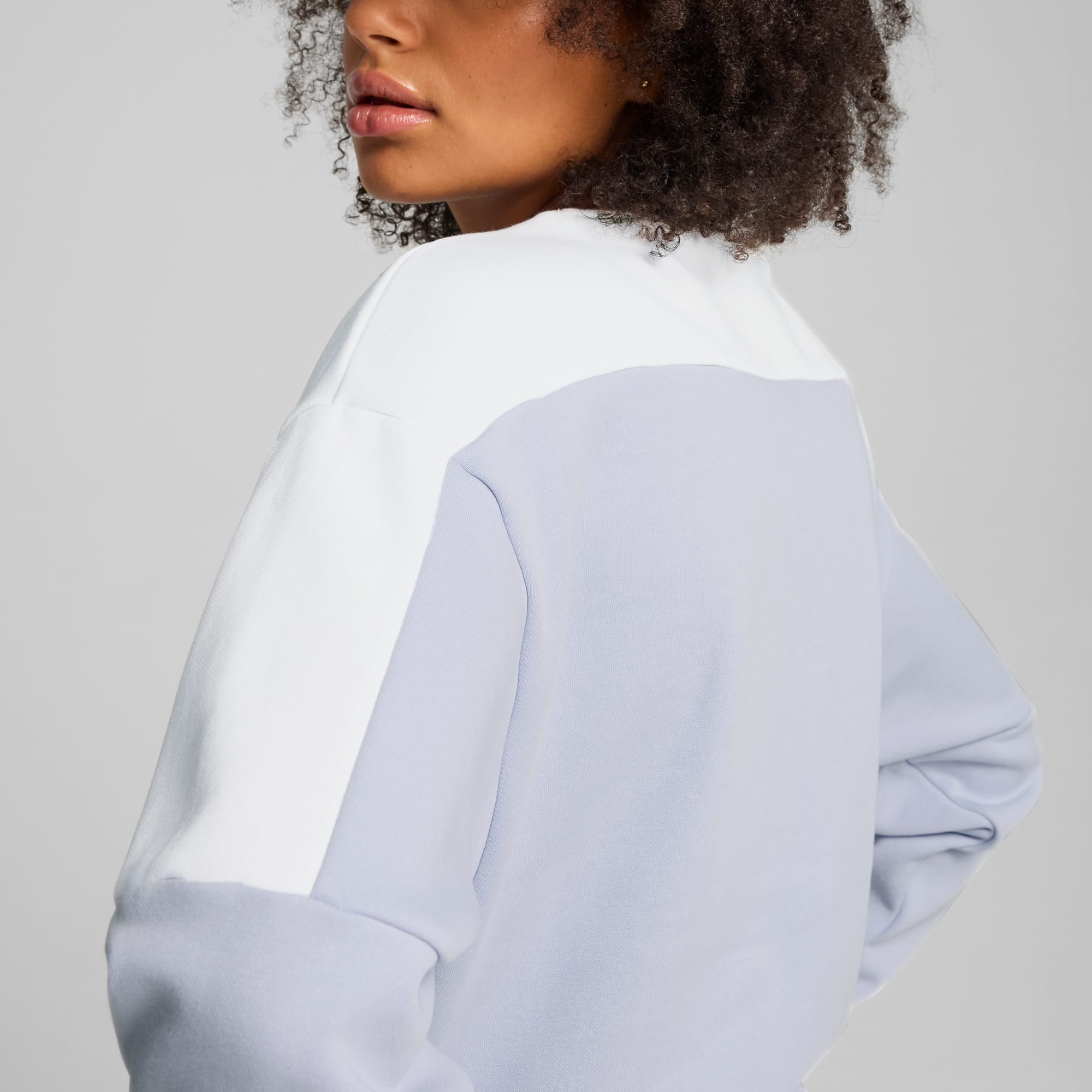 Una modella posa su uno sfondo grigio, indossando una felpa color block bianca e blu.