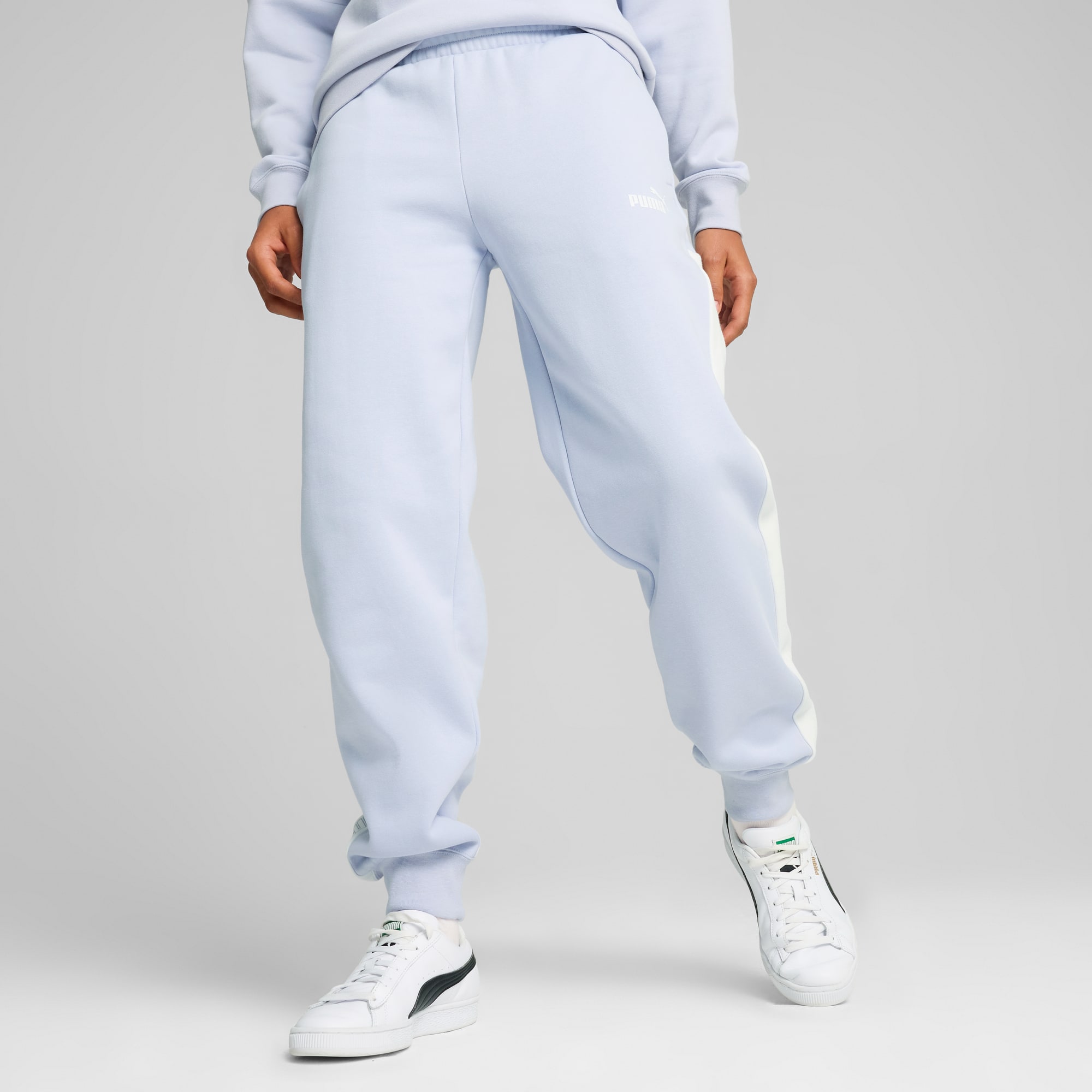 Op grijs draagt een model een lichtblauwe broek en sneakers, poserend met gespreide benen.
