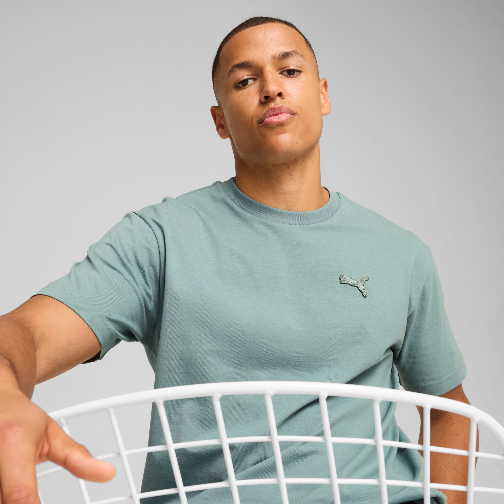 Un mannequin pose sur fond gris, portant un t-shirt vert avec un logo.