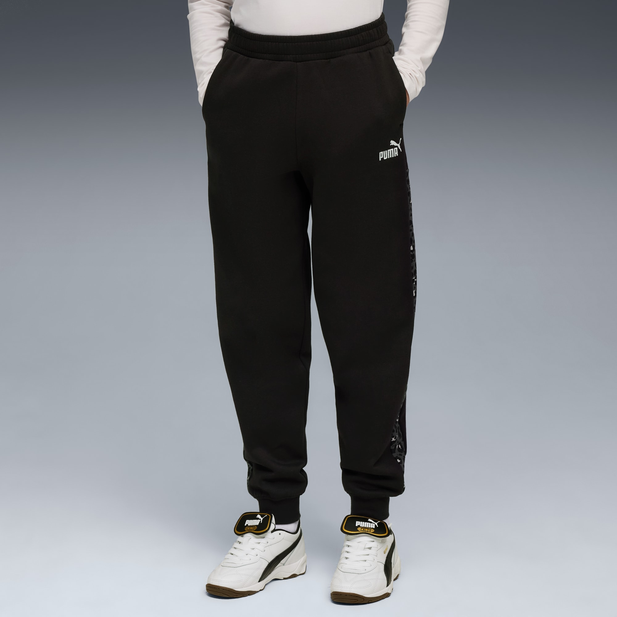 Un modello posa su sfondo grigio, mettendo in mostra pantaloni neri e scarpe da ginnastica bianche.