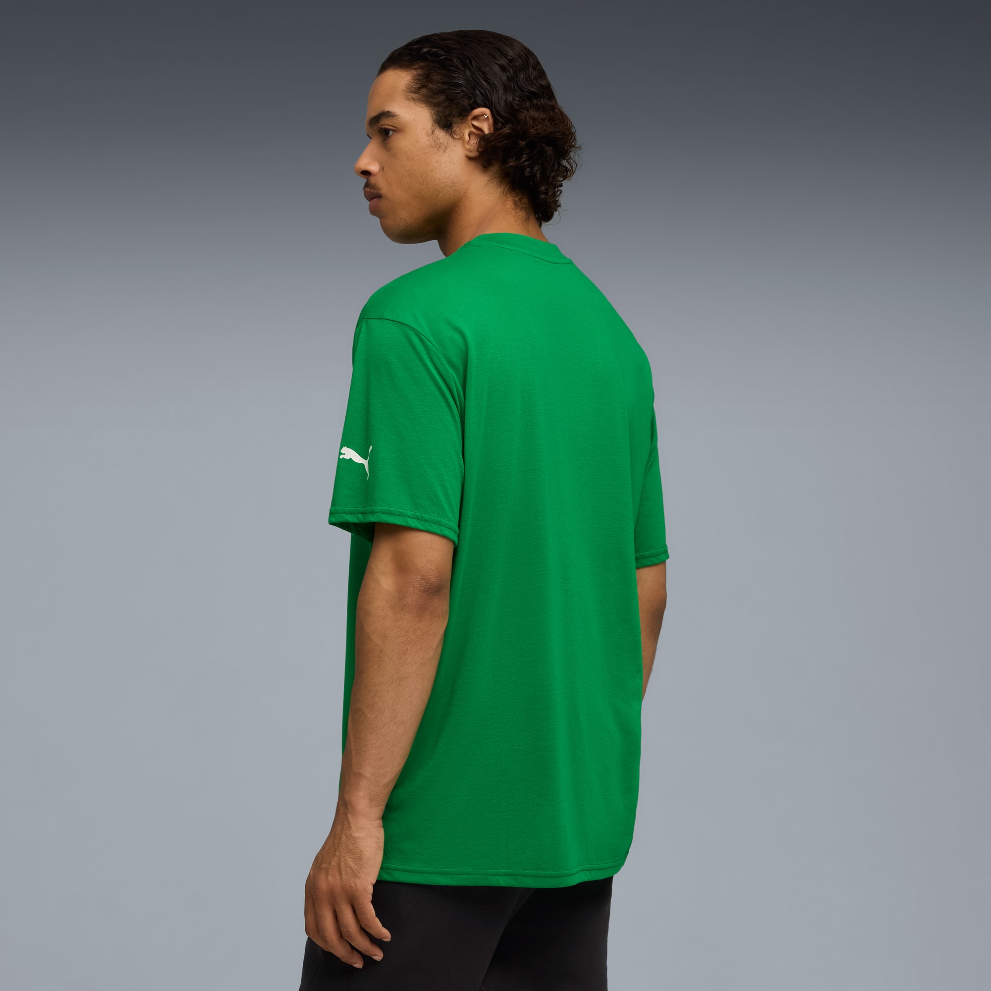 Un modello in t-shirt verde e pantaloni neri posa su sfondo grigio.