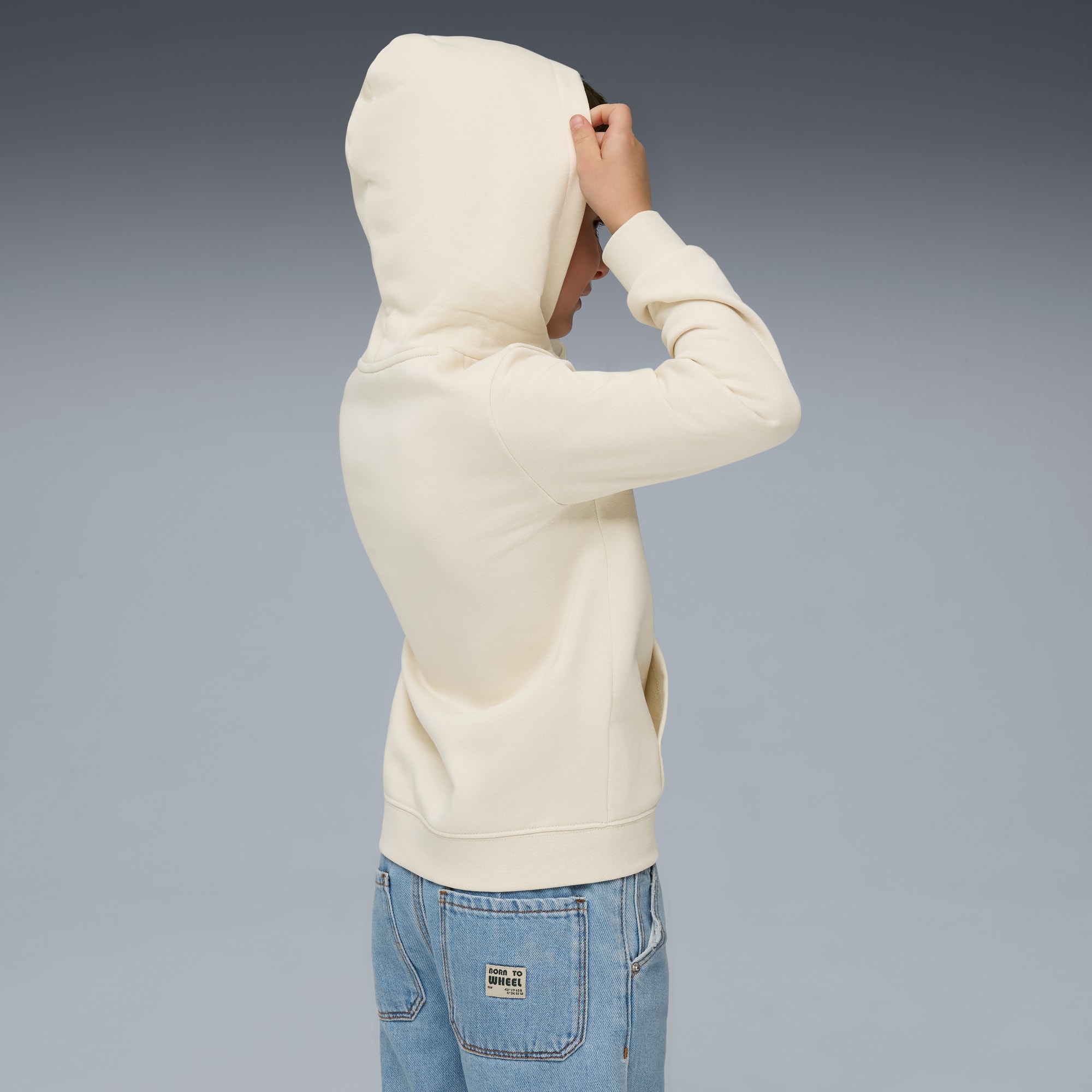 Sur fond gris, un mannequin ajuste la capuche de son sweat-shirt à capuche crème.