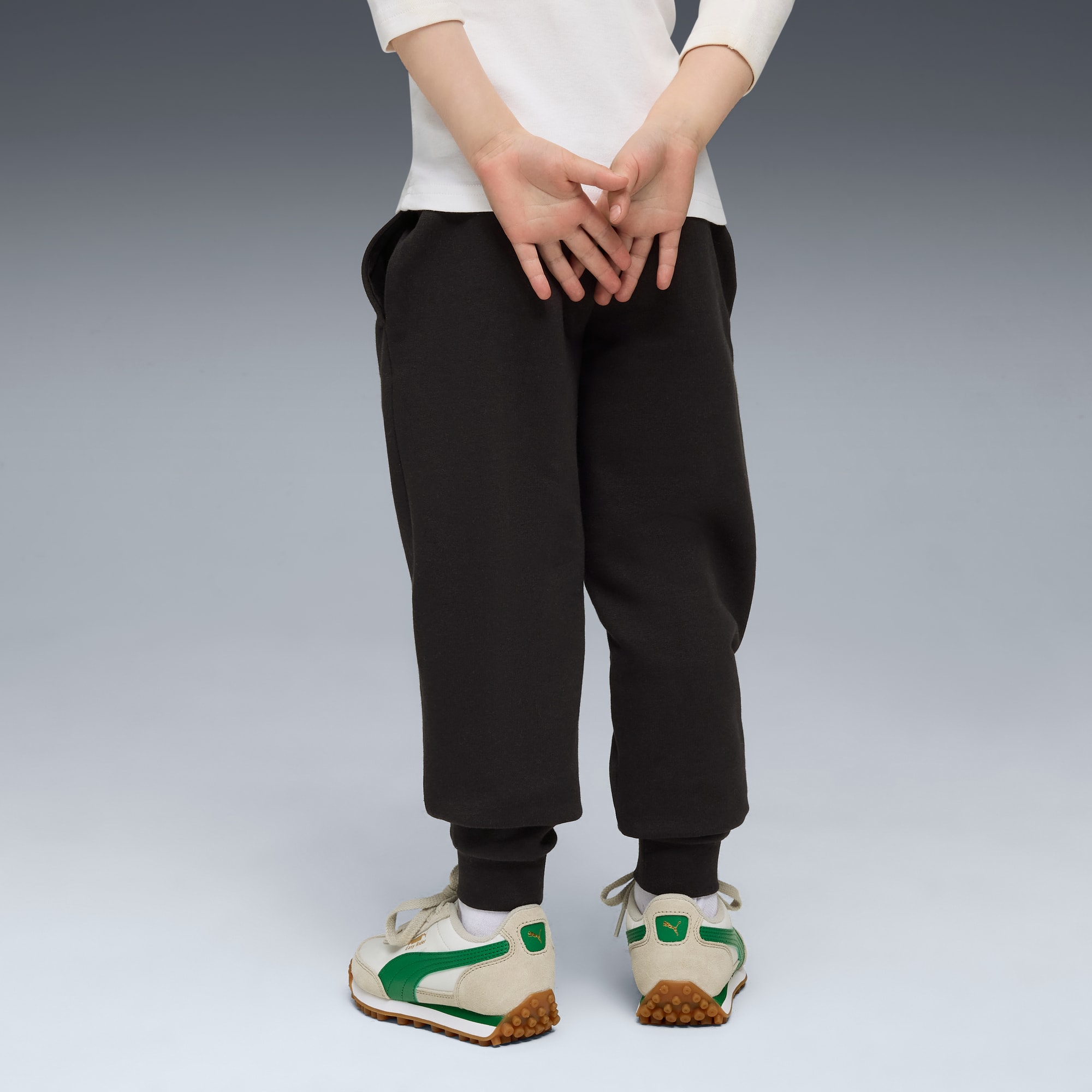 Un modello di spalle su sfondo grigio indossa pantaloni da jogging neri e scarpe da ginnastica rétro.