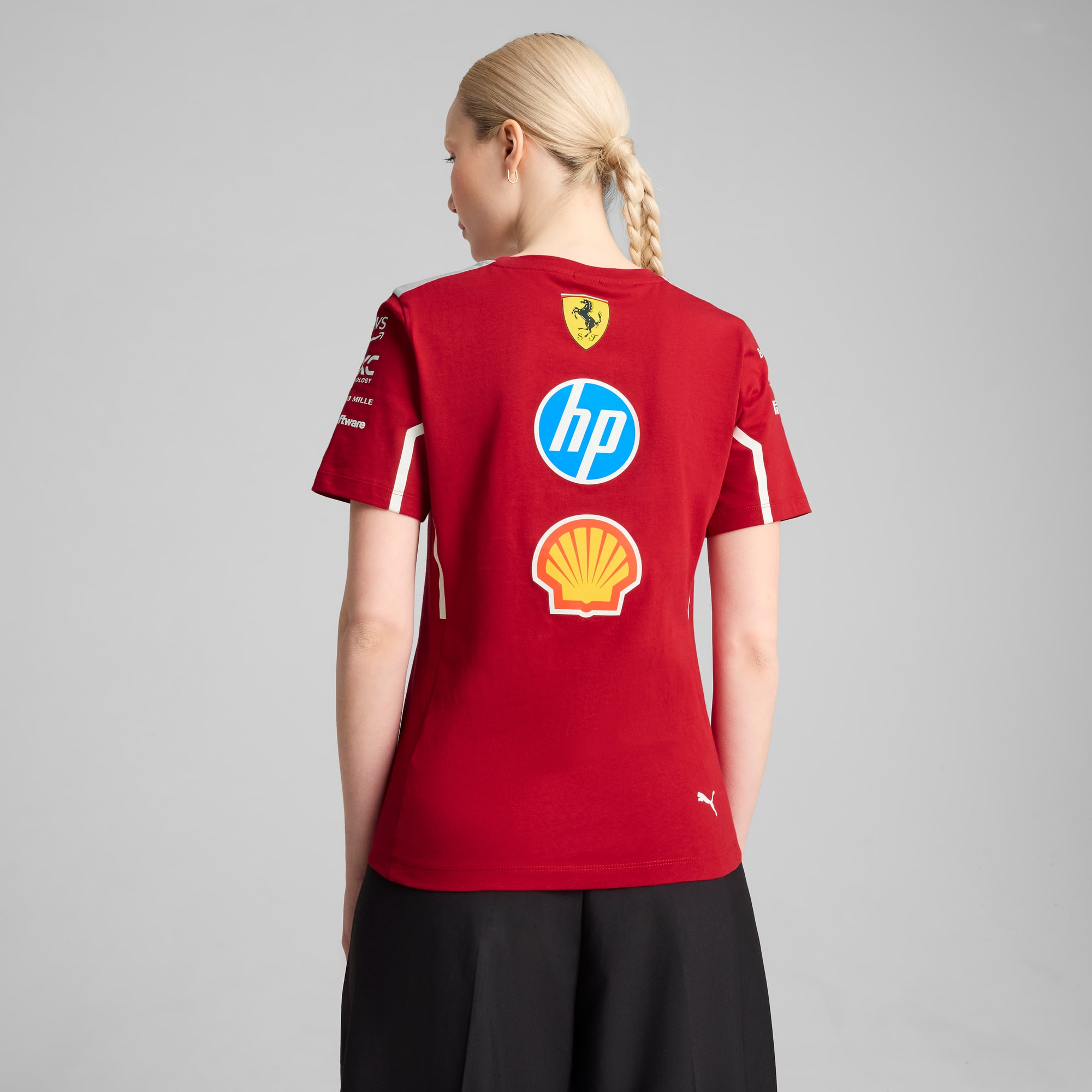 Vor grauem Hintergrund trägt ein Model ein rotes T-Shirt mit Logos und eine schwarze Hose.