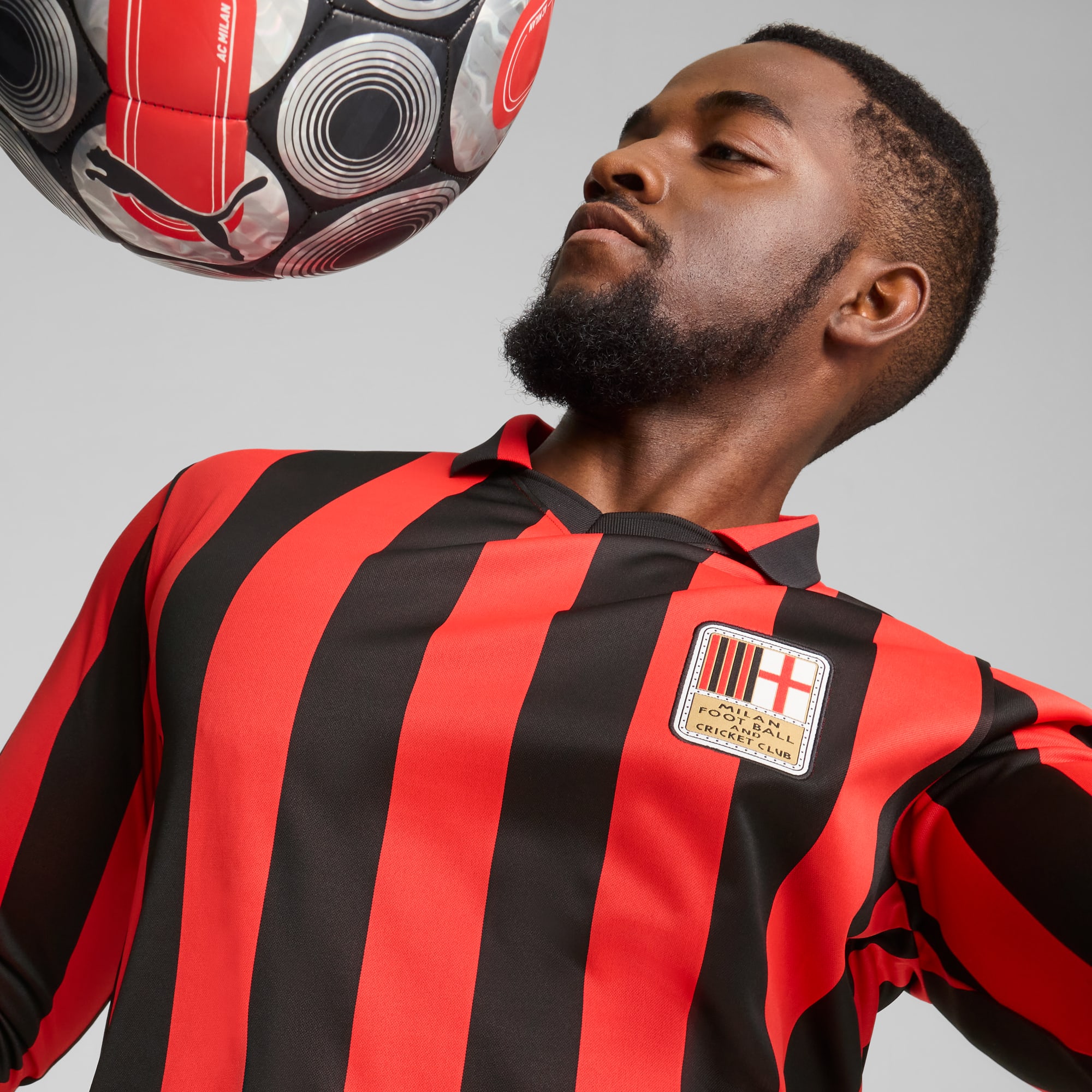 Sobre fondo gris, un modelo con camiseta a rayas rojas y negras mira un balón.