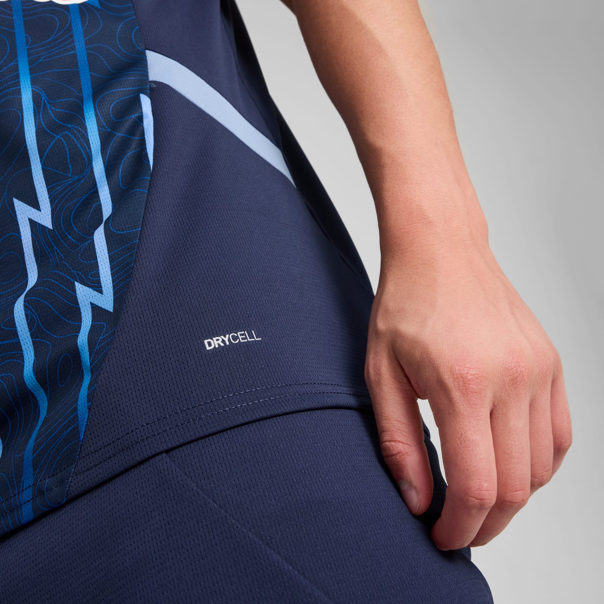 Close-up van een persoon met een blauw shirt met patroon en 'DRYCELL'-tekst op een grijze achtergrond.