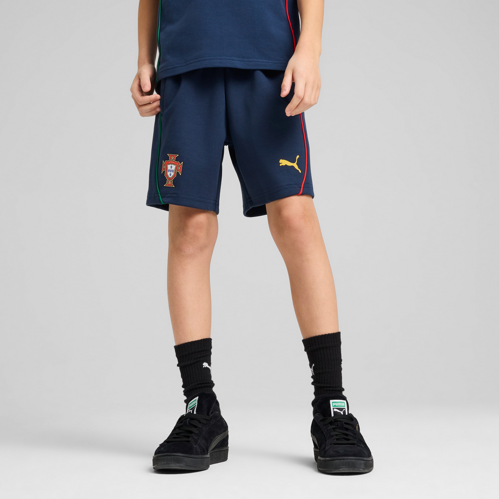 On grey, a child models navy shorts with Portugal's emblem, paired with black socks and shoes.