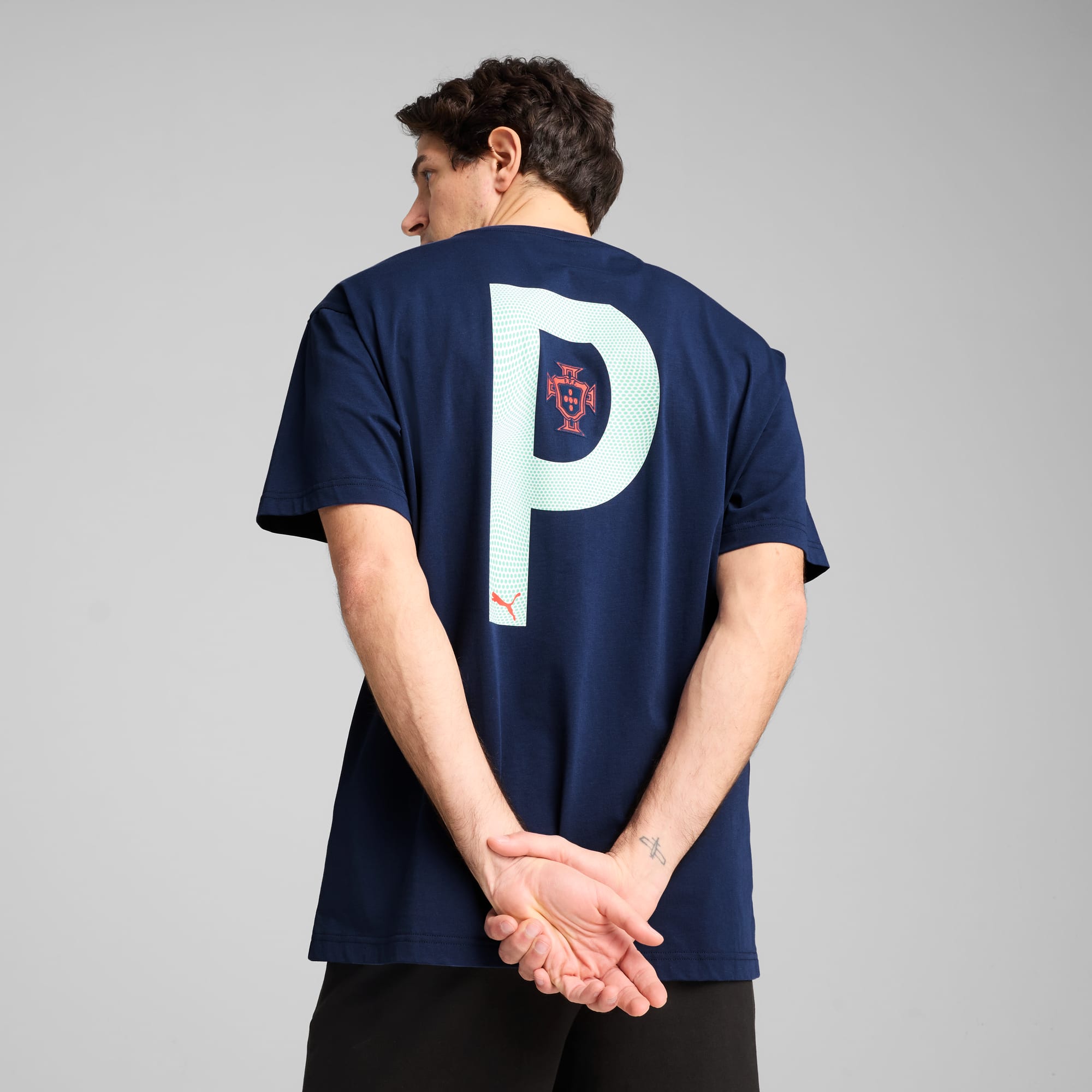 Un mannequin, dos au fond gris, porte un t-shirt bleu marine avec un grand 'P' et un emblème.