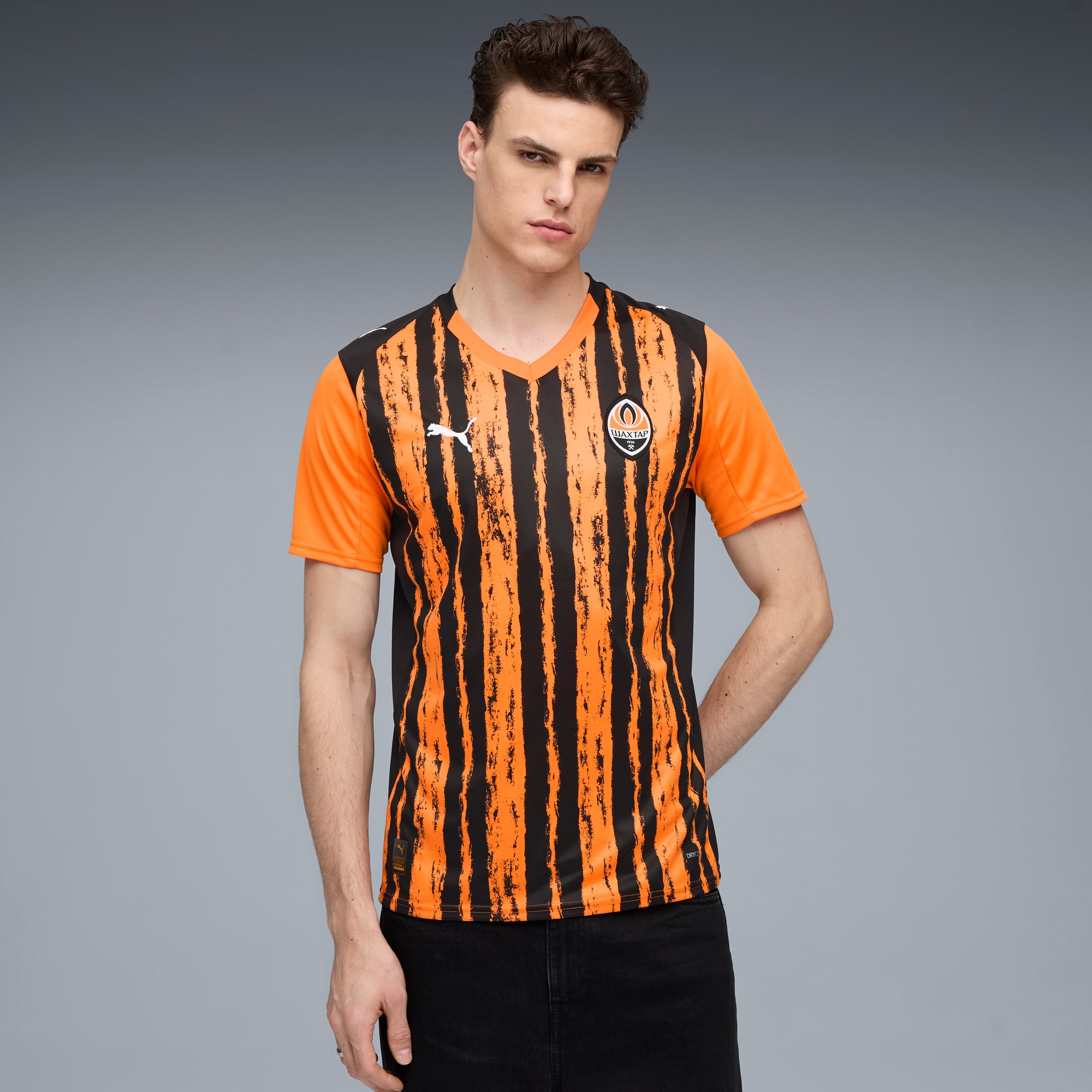 Sur fond gris, un mannequin porte un maillot de football rayé orange et noir.