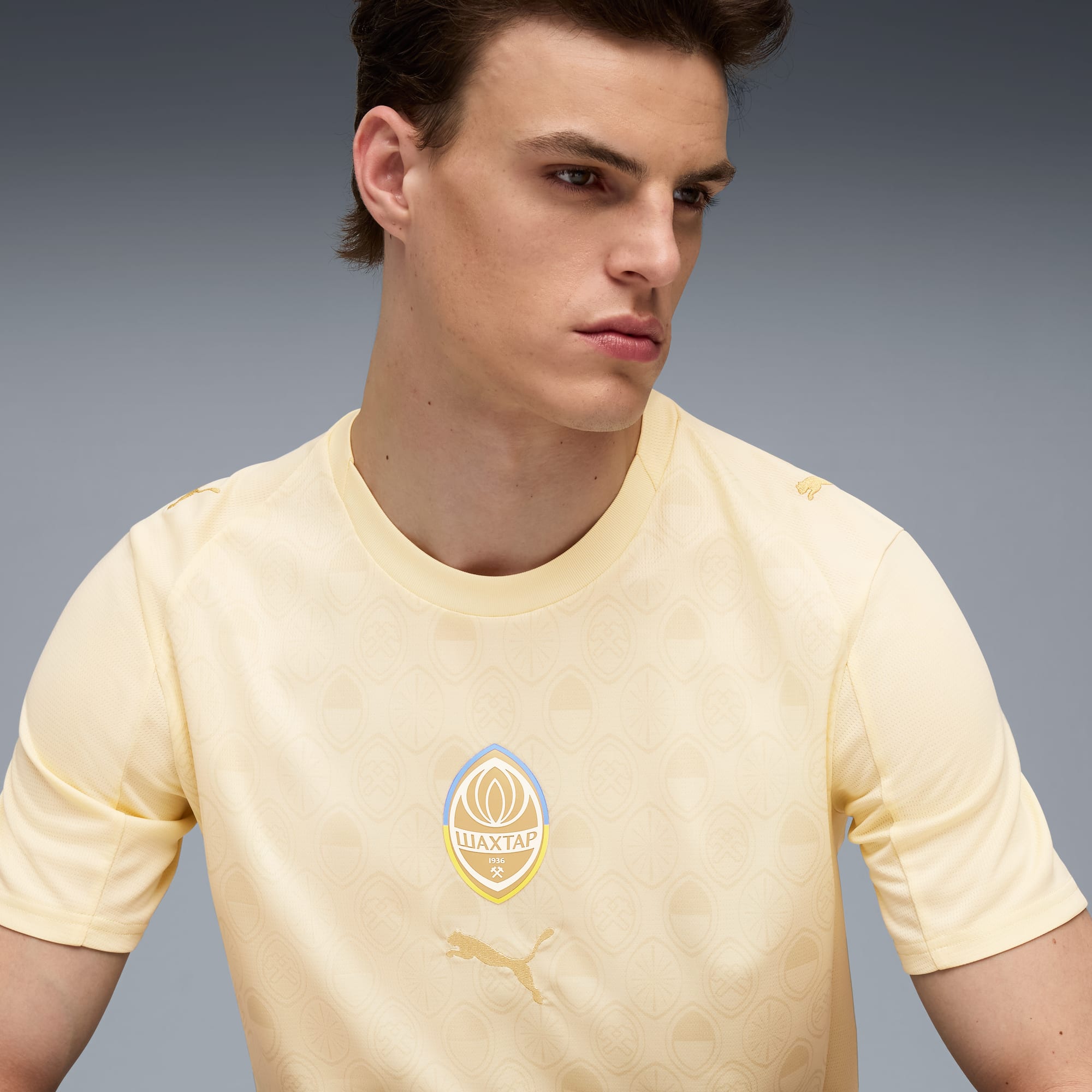 Een model poseert tegen een grijze achtergrond in een lichtgeel T-shirt met patroon.