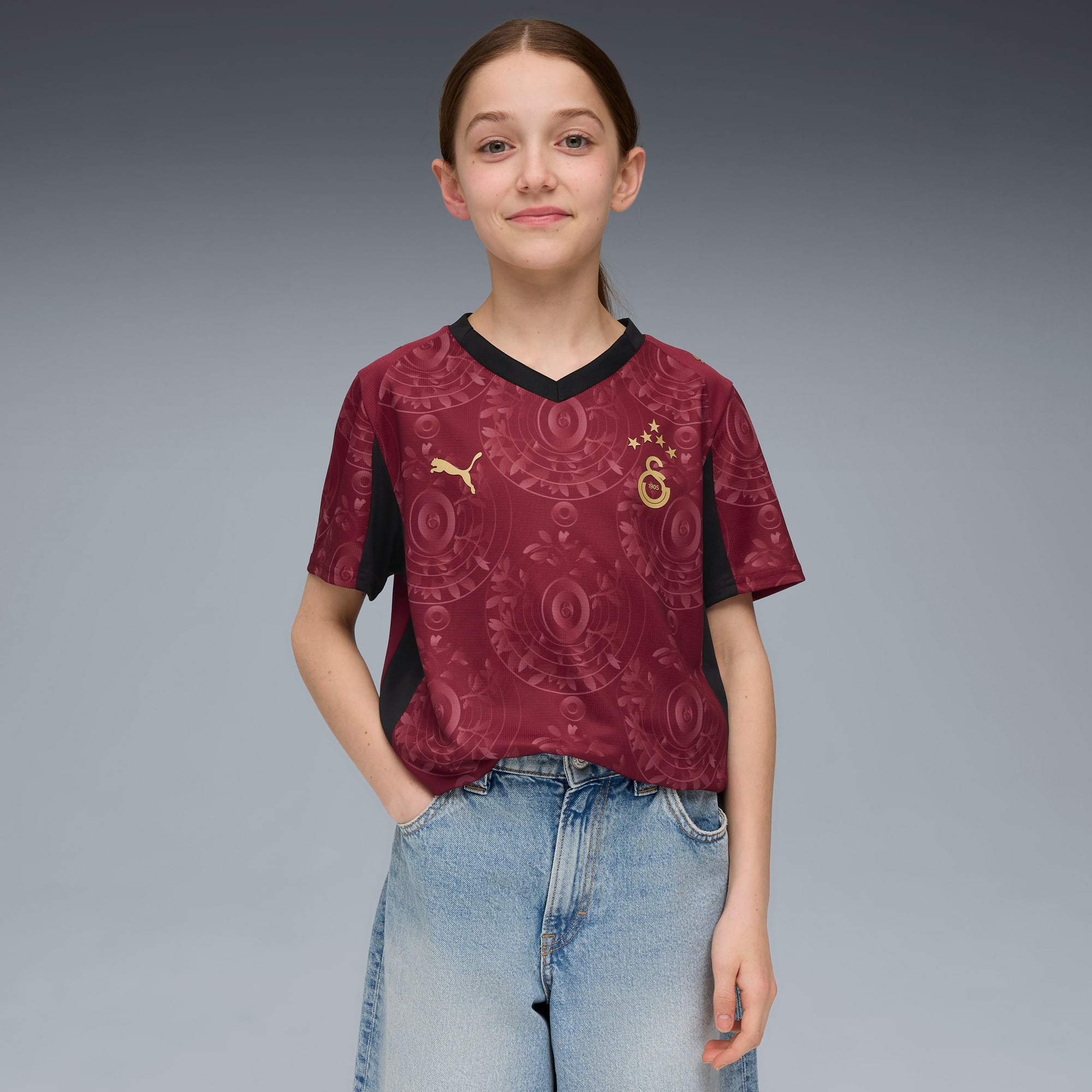Un mannequin pose sur fond gris, portant un haut bordeaux à motifs et un short en jean bleu.