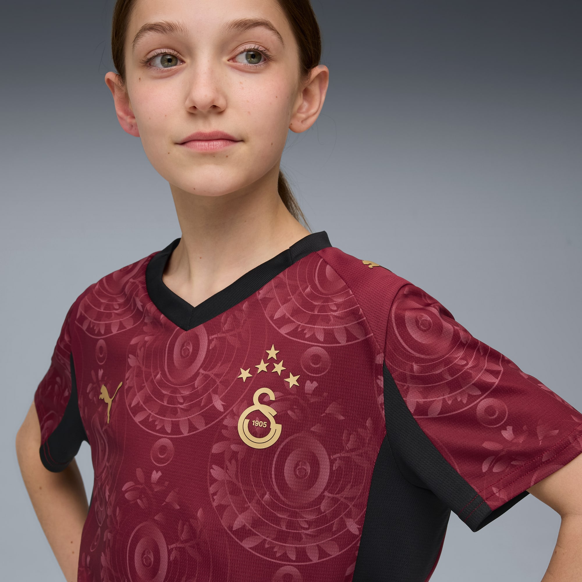 Sur fond gris, un mannequin pose avec un maillot de sport bordeaux à motifs.